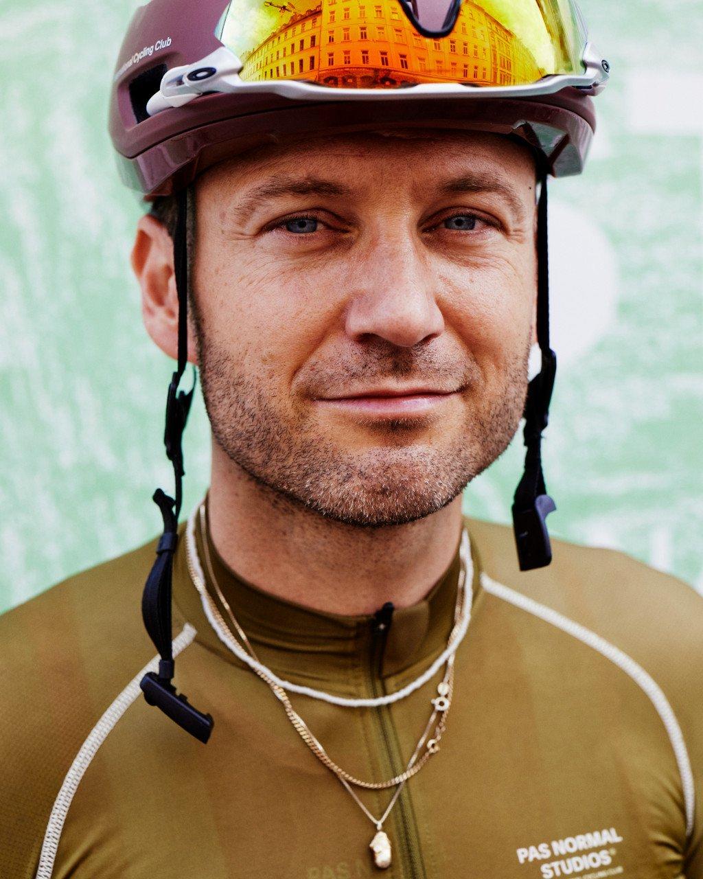 Model wearing brown cycling jersey with white piping and cycling helmet with yellow-tinted visor