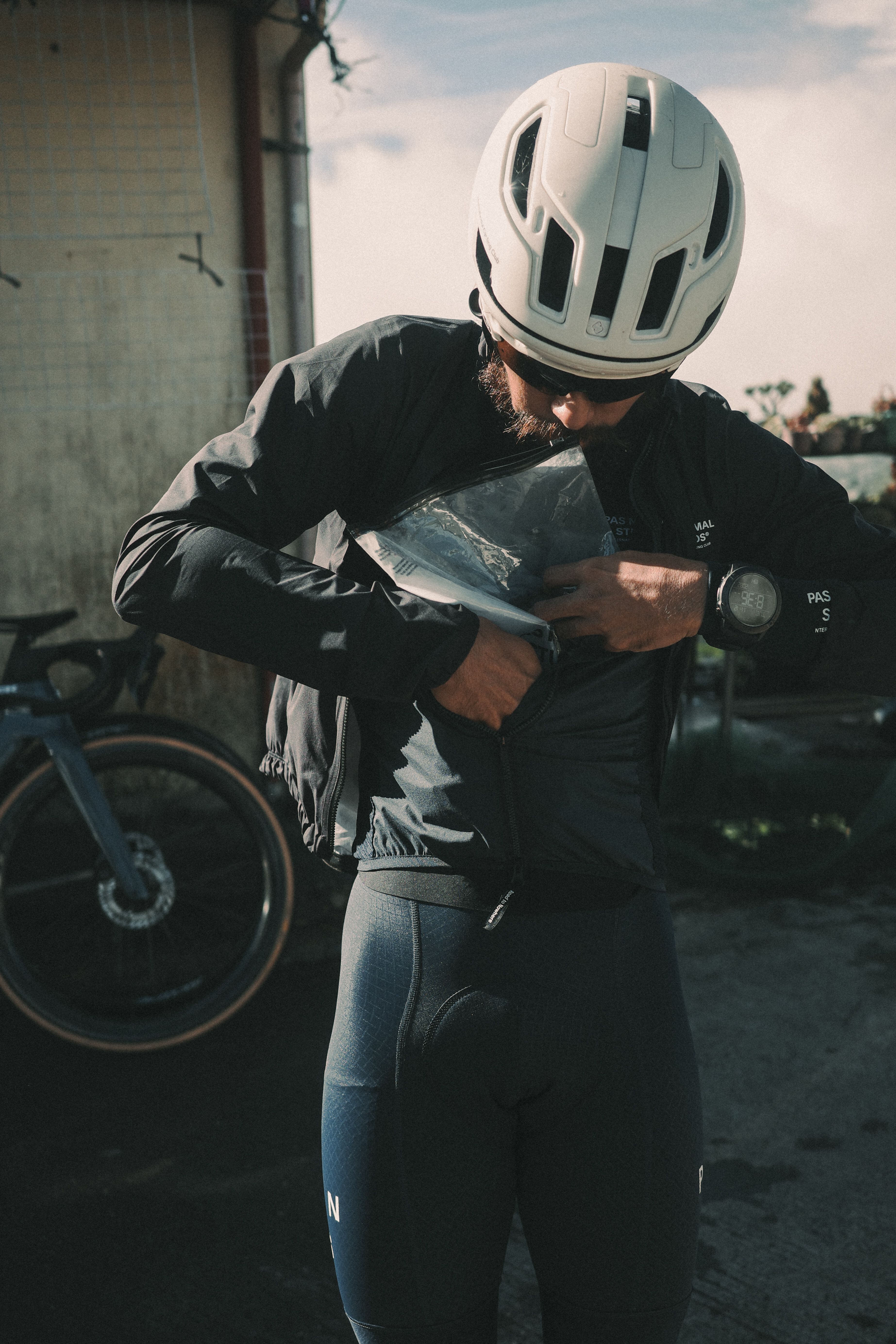 Model wearing black cycling jacket and grey bib tights, white helmet, checking map in urban setting