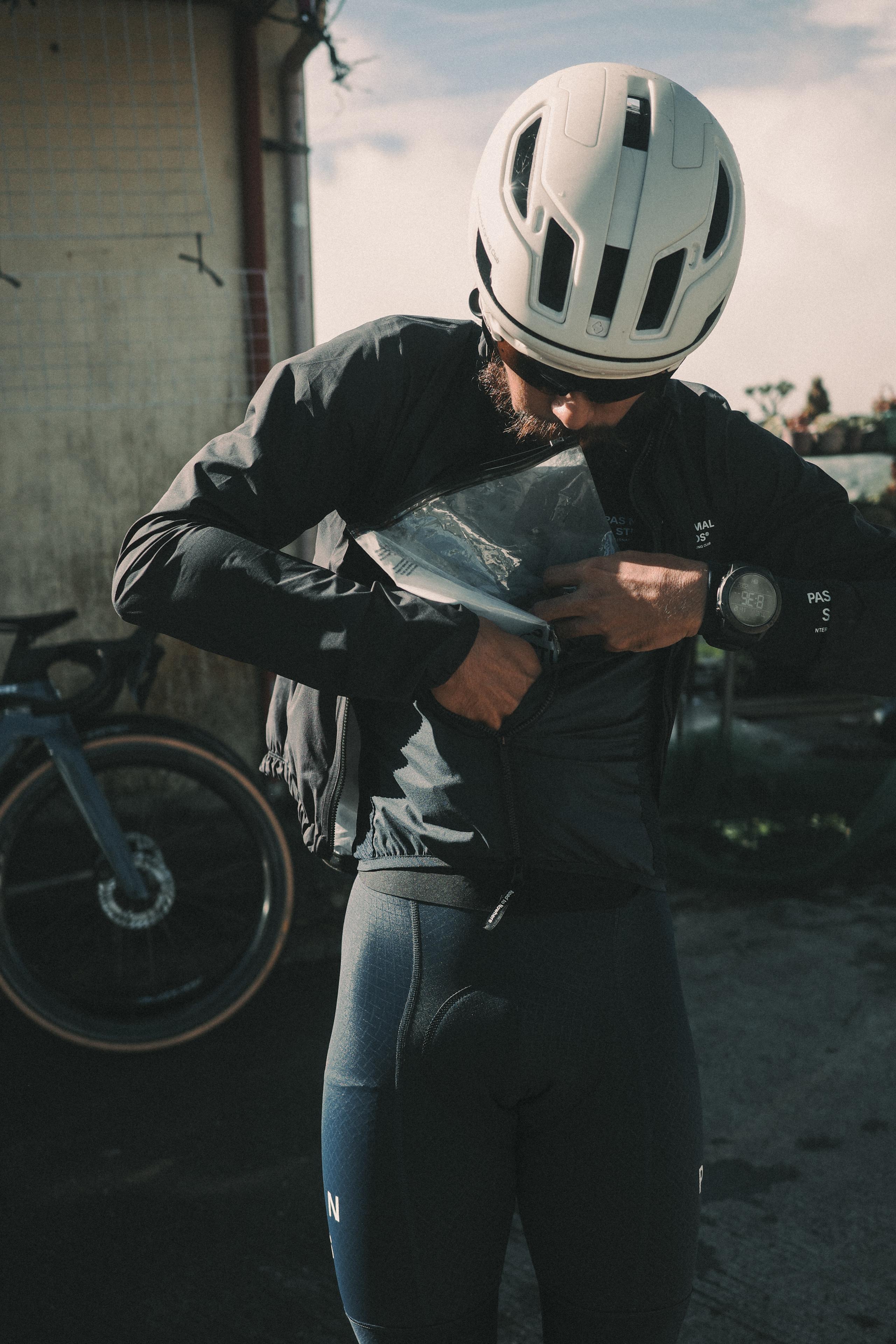 Model wearing black cycling jacket and grey bib tights, white helmet, checking map in urban setting