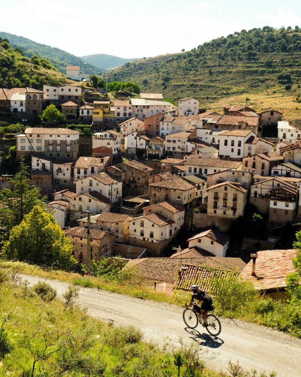 Cyclist riding through Mediterranean hillside village with stone buildings and terracotta roofs