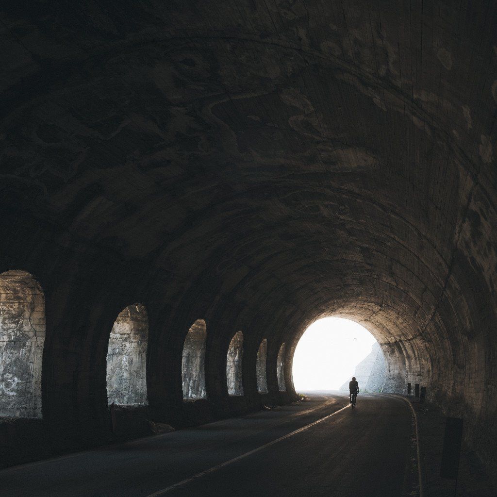 Cyclist silhouette in stone tunnel with arched openings and bright exit