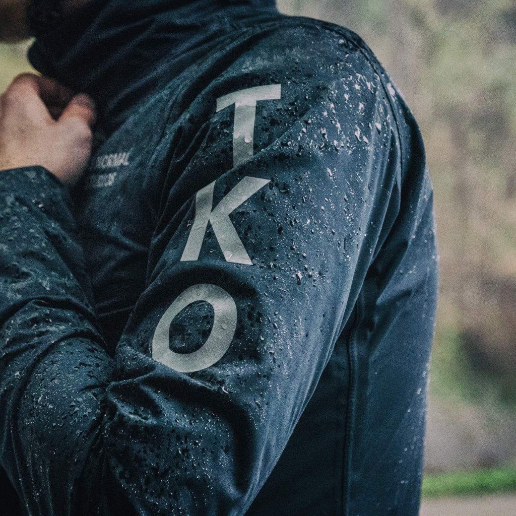 Model wearing navy cycling jacket with large text graphics, covered in water droplets