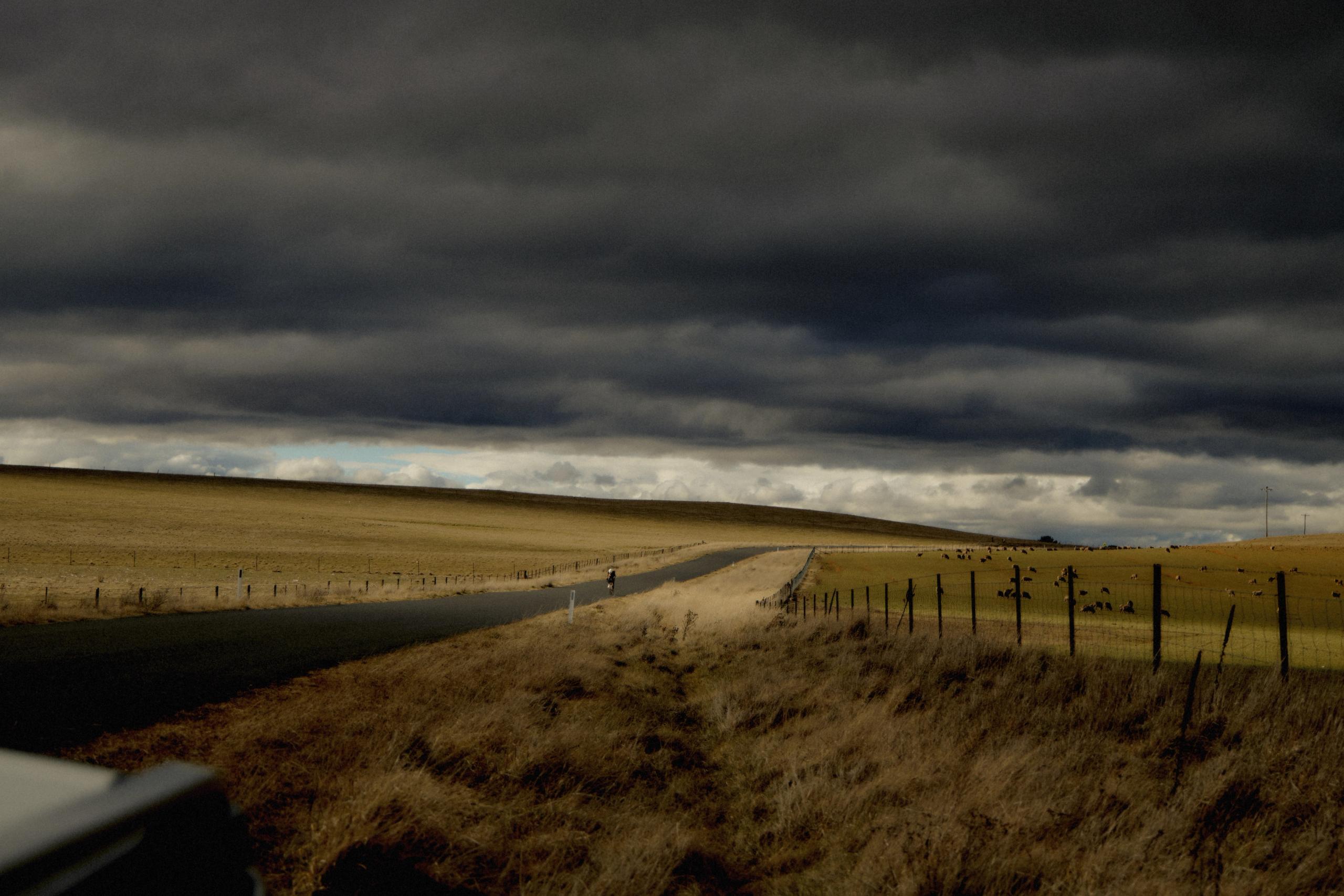 Rural road through golden fields under dramatic storm clouds