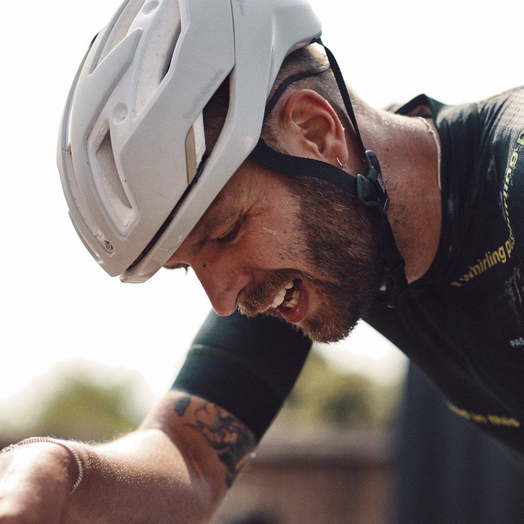 Model wearing white cycling helmet and black jersey with sunglasses, looking down outdoors