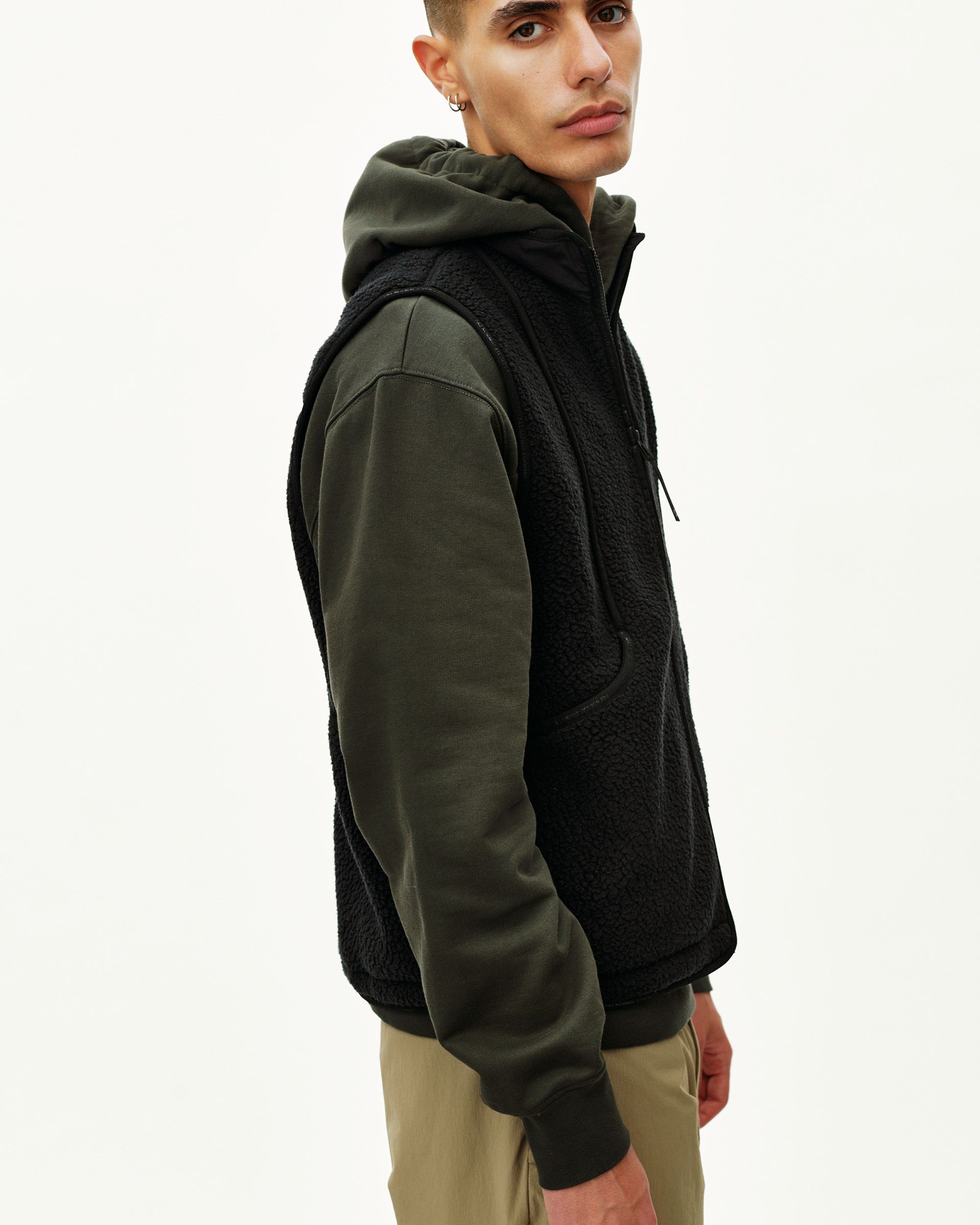 Black Off-Race Pile Fleece vest on model, three-quarter side view with sherpa body and army green hoodie layered beneath