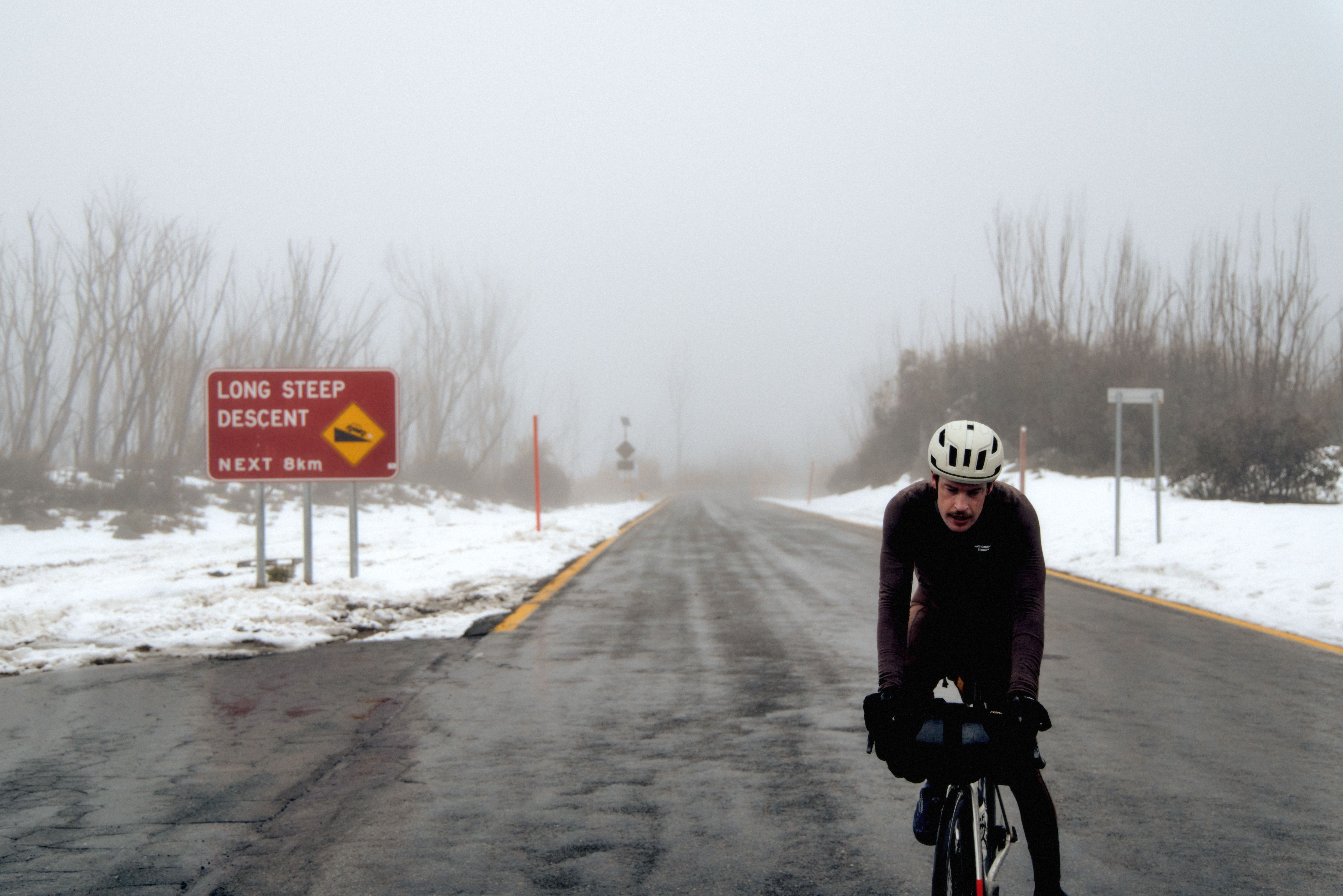 Model wearing dark cycling gear on snowy winter road in aerodynamic position