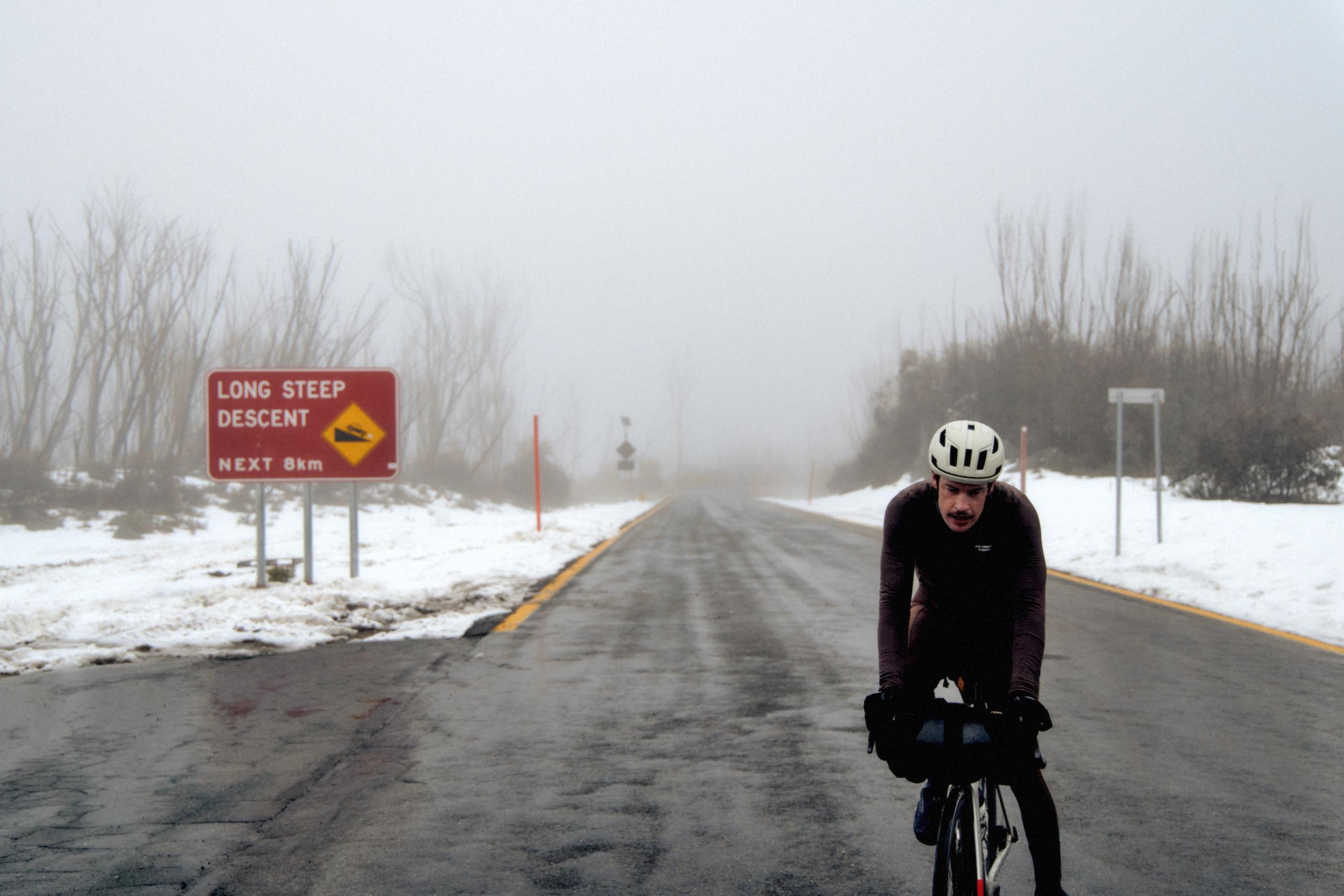 Model wearing dark cycling gear on snowy winter road in aerodynamic position