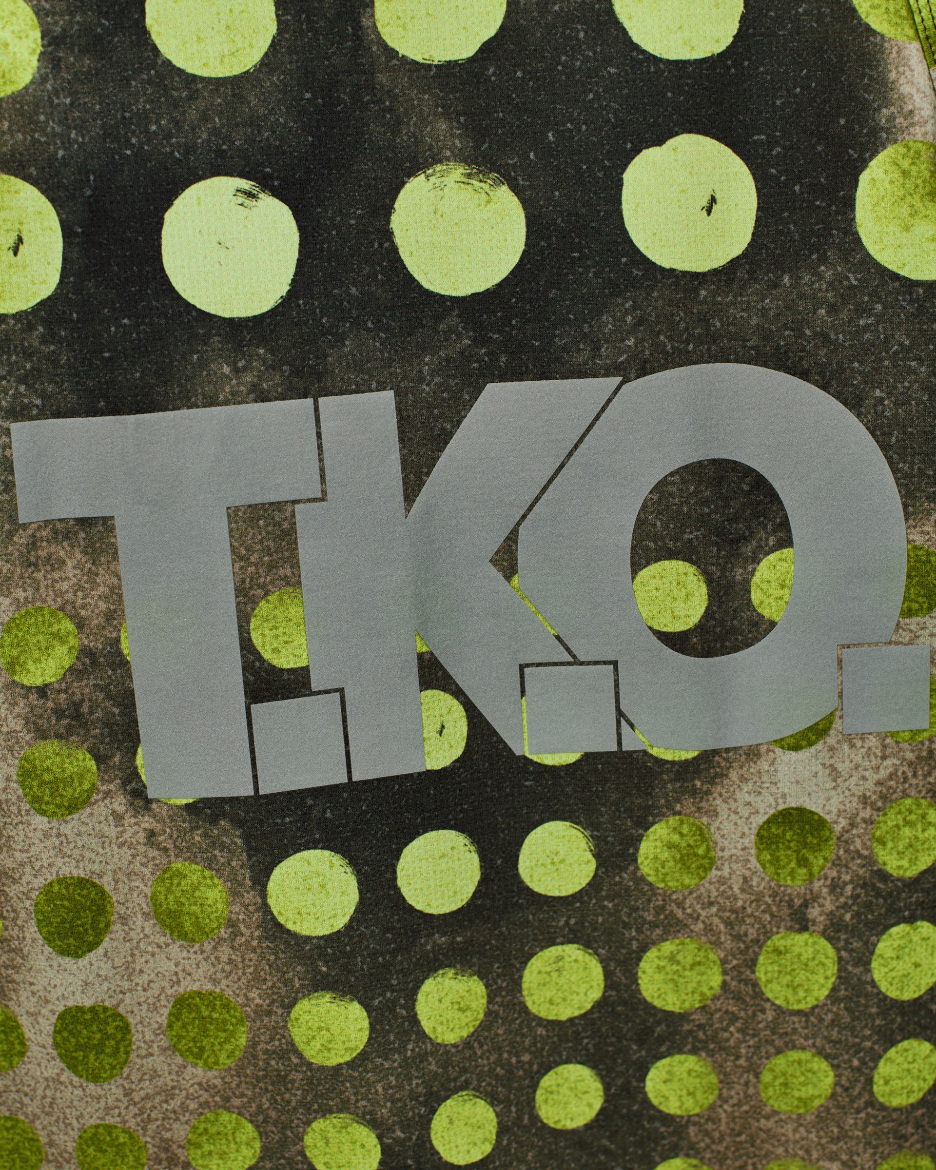 Green T.K.O. Balance singlet, detail view with polka dot print and grey T.K.O. logo