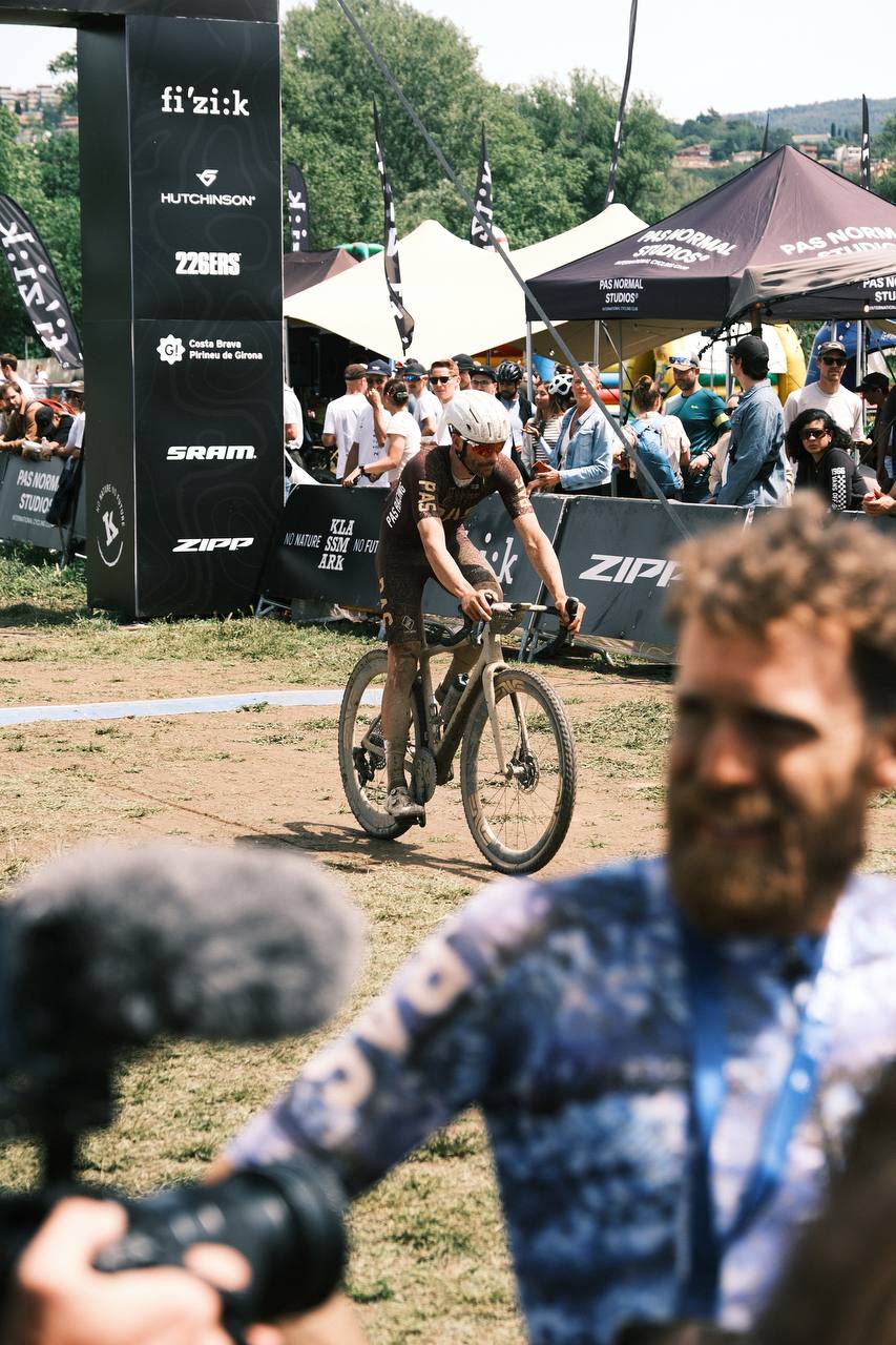 Cyclist in racing position on gravel bike at outdoor cycling event with spectators and sponsor tents