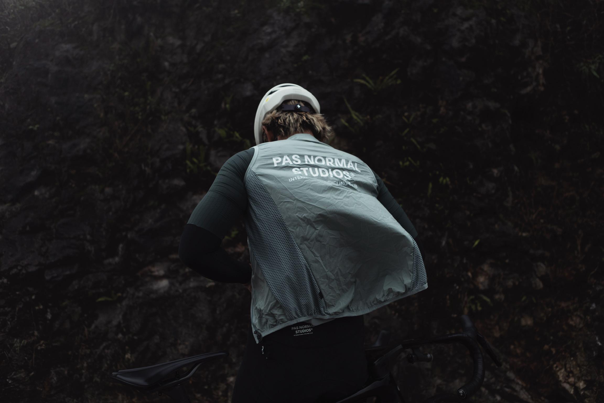 Model wearing grey cycling vest with back branding, shown from behind in natural forest setting