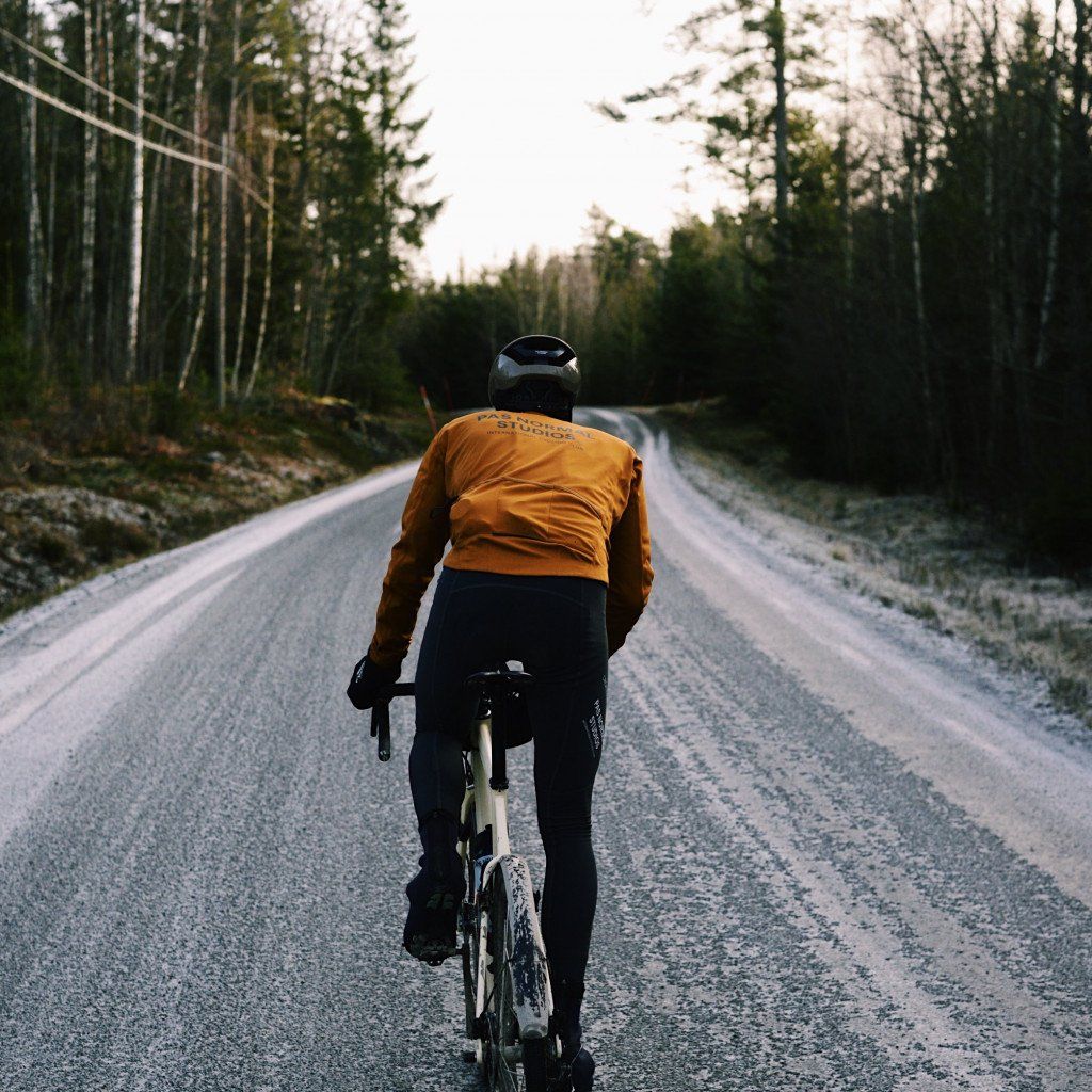 Model wearing orange long-sleeve jersey and black tights cycling on forest road