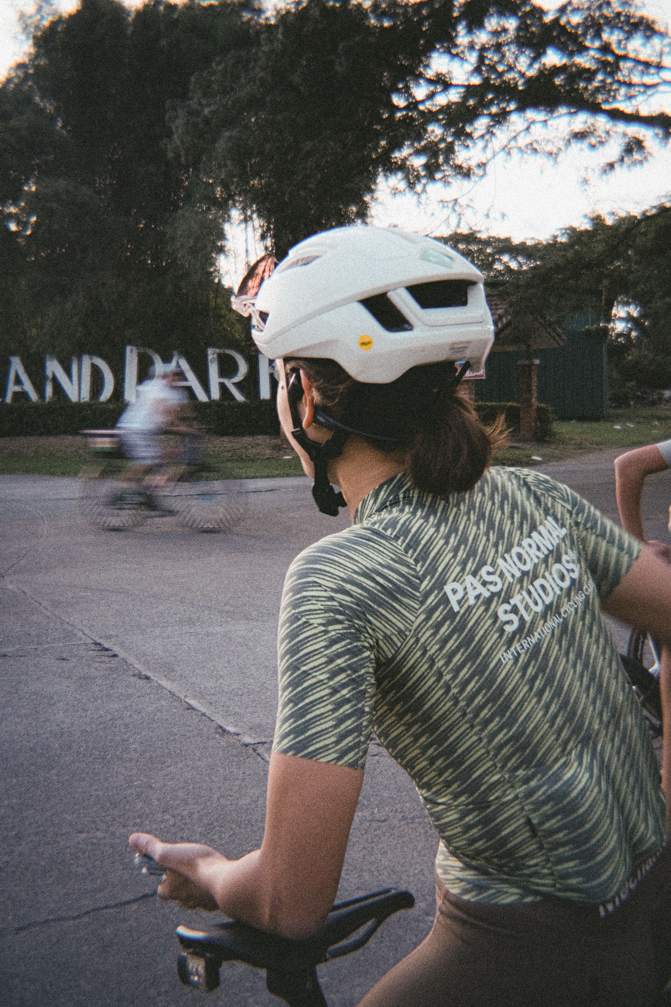 Model wearing green striped jersey with back branding, white helmet, sitting outdoors