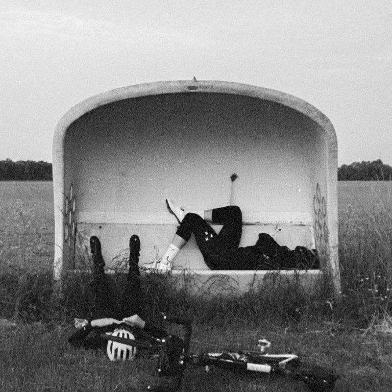 Cyclist resting in concrete underpass with bicycle and gear in foreground, black and white photograph