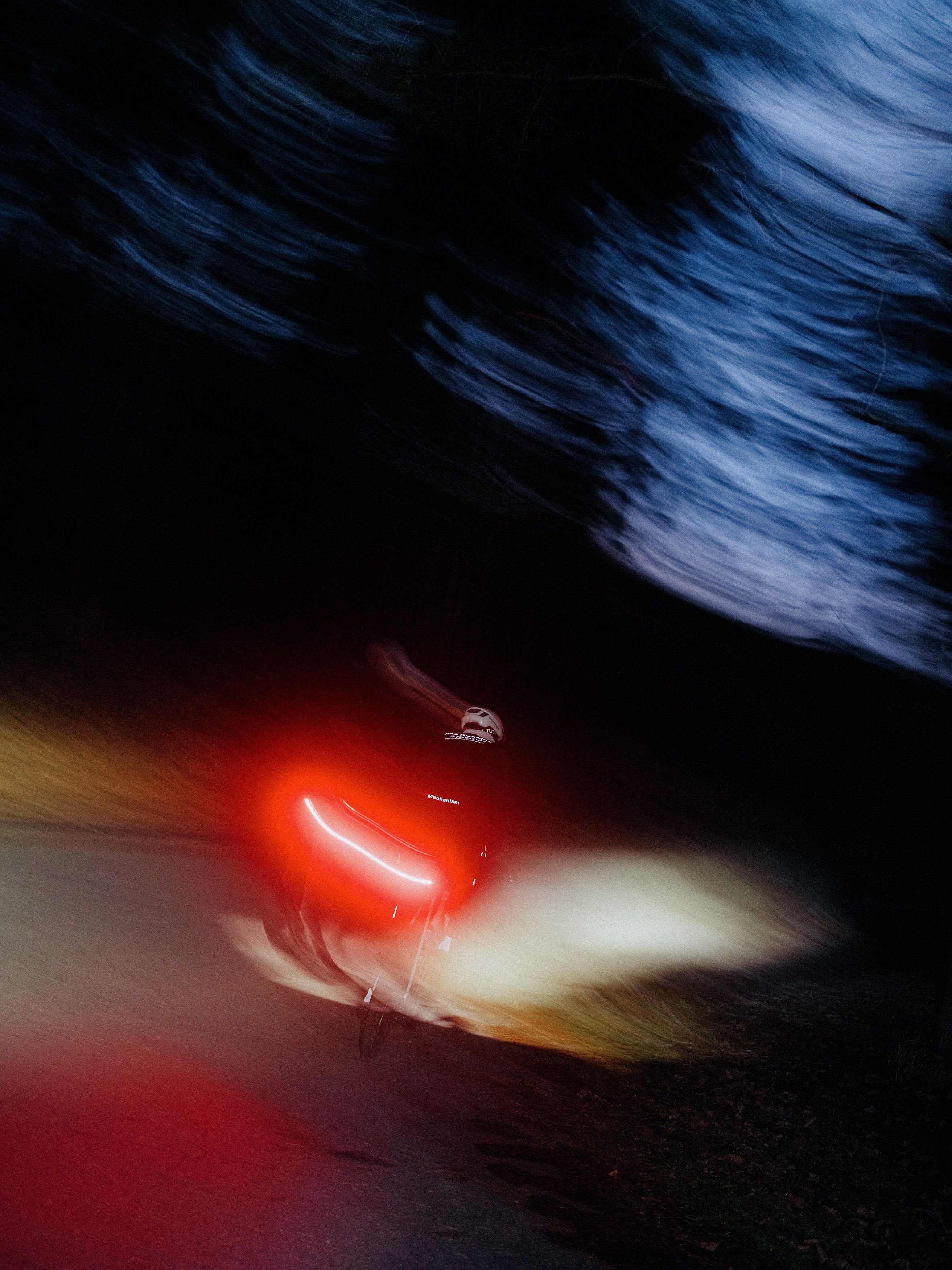Cyclist with red rear light riding through dark forest with motion blur
