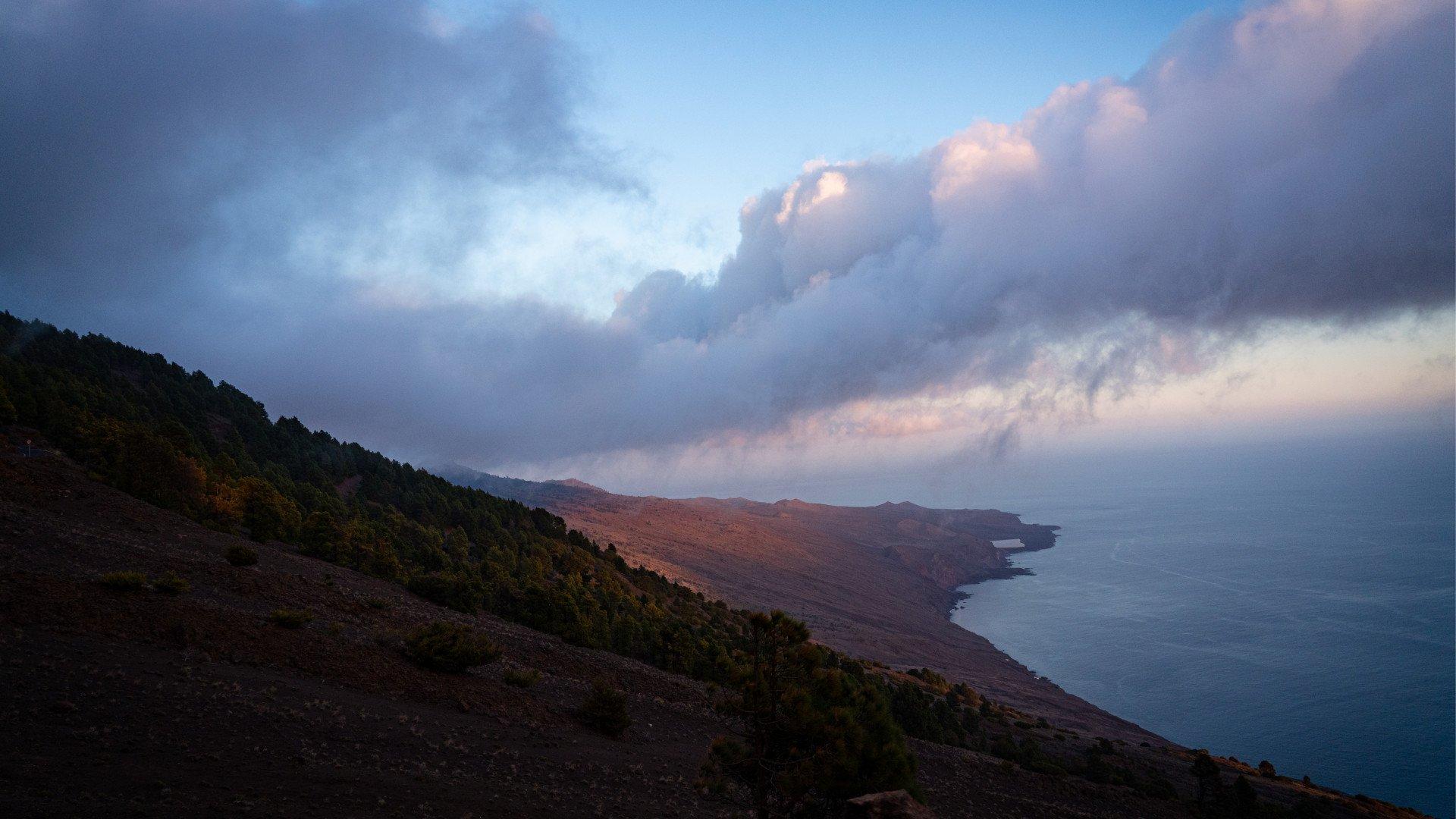 Dramatic coastal landscape with rugged hills meeting ocean under stormy twilight sky