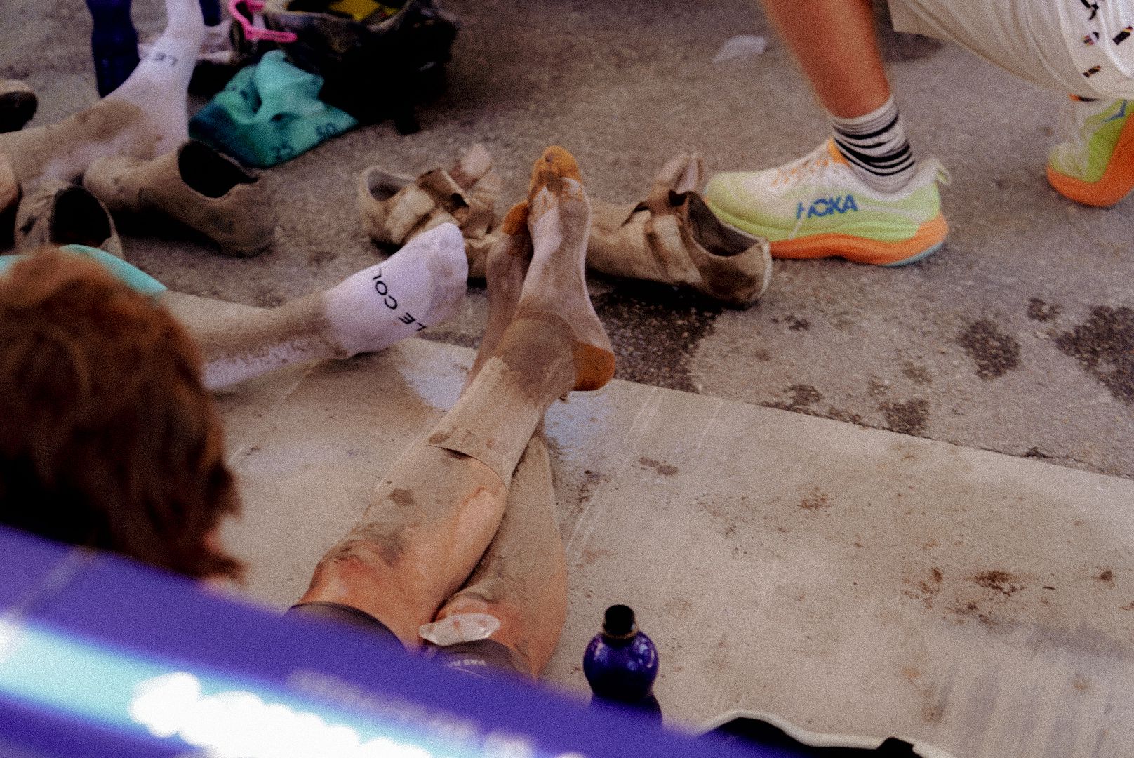 Cyclists resting on ground after gravel race with white socks and running shoes visible