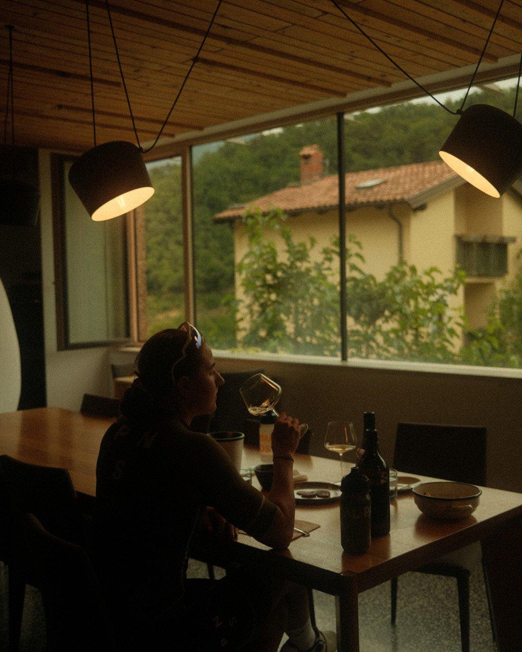 Model wearing dark clothing enjoying wine at dining table in modern interior with mountain view