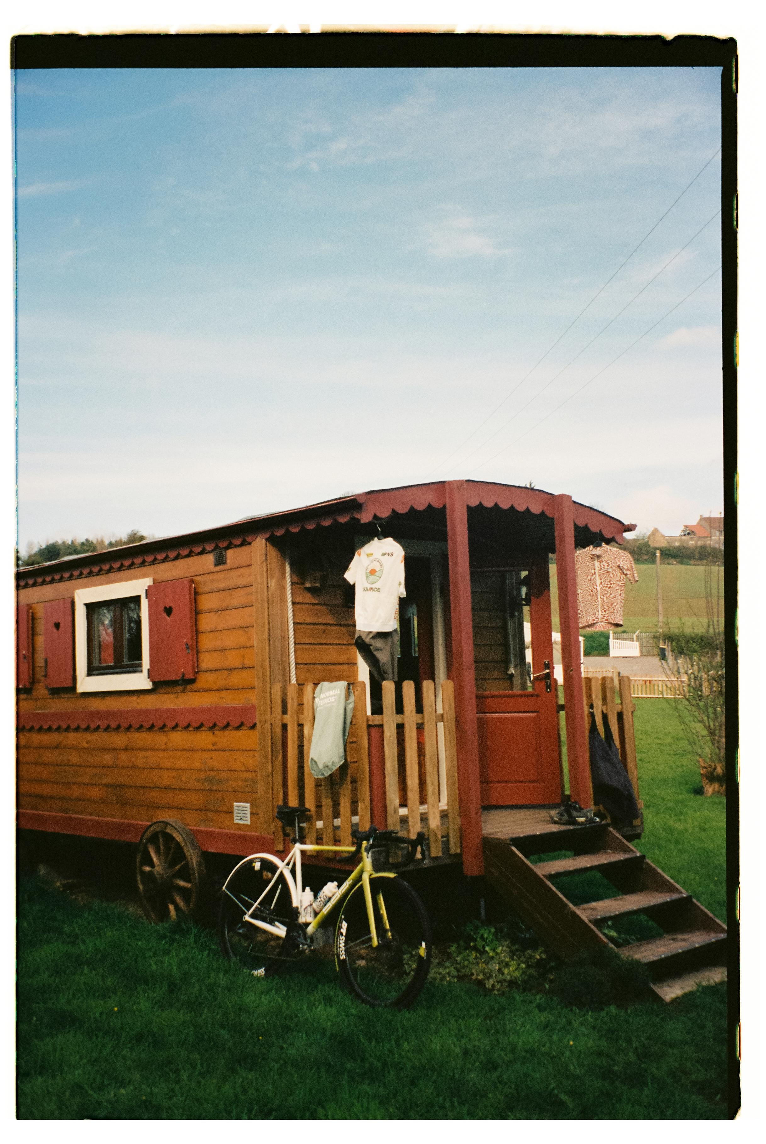 Wooden caravan with cycling apparel hanging outside and yellow bicycle parked in front
