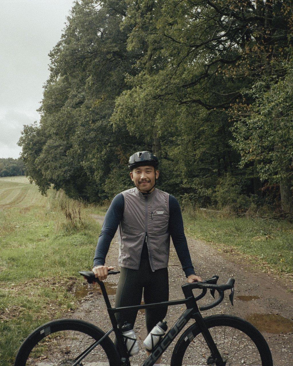 Model wearing grey cycling vest and dark base layer with bike on country path