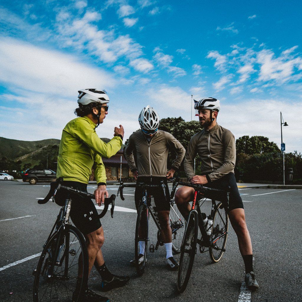 Three cyclists in green and olive cycling jackets with their bikes gathered on road in Sonoma countryside