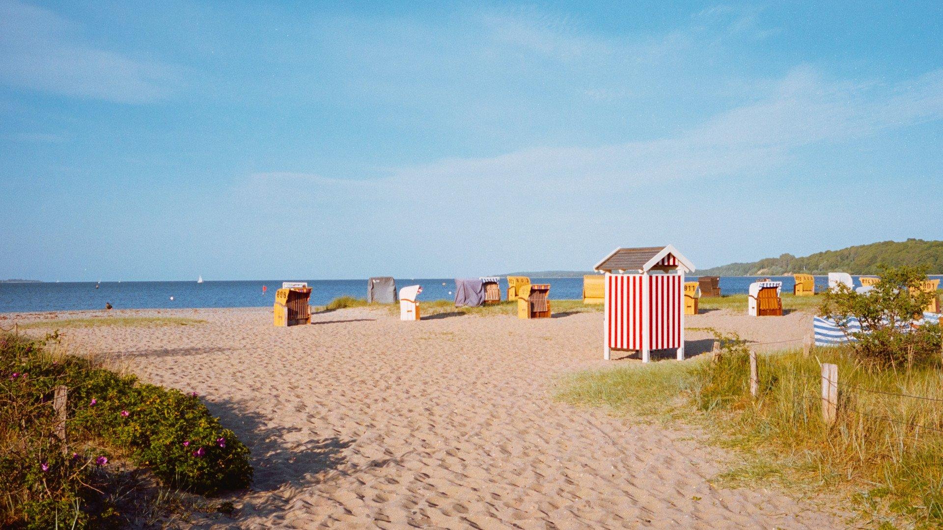 Beach scene with colorful striped cabanas and wicker beach chairs on sandy shore
