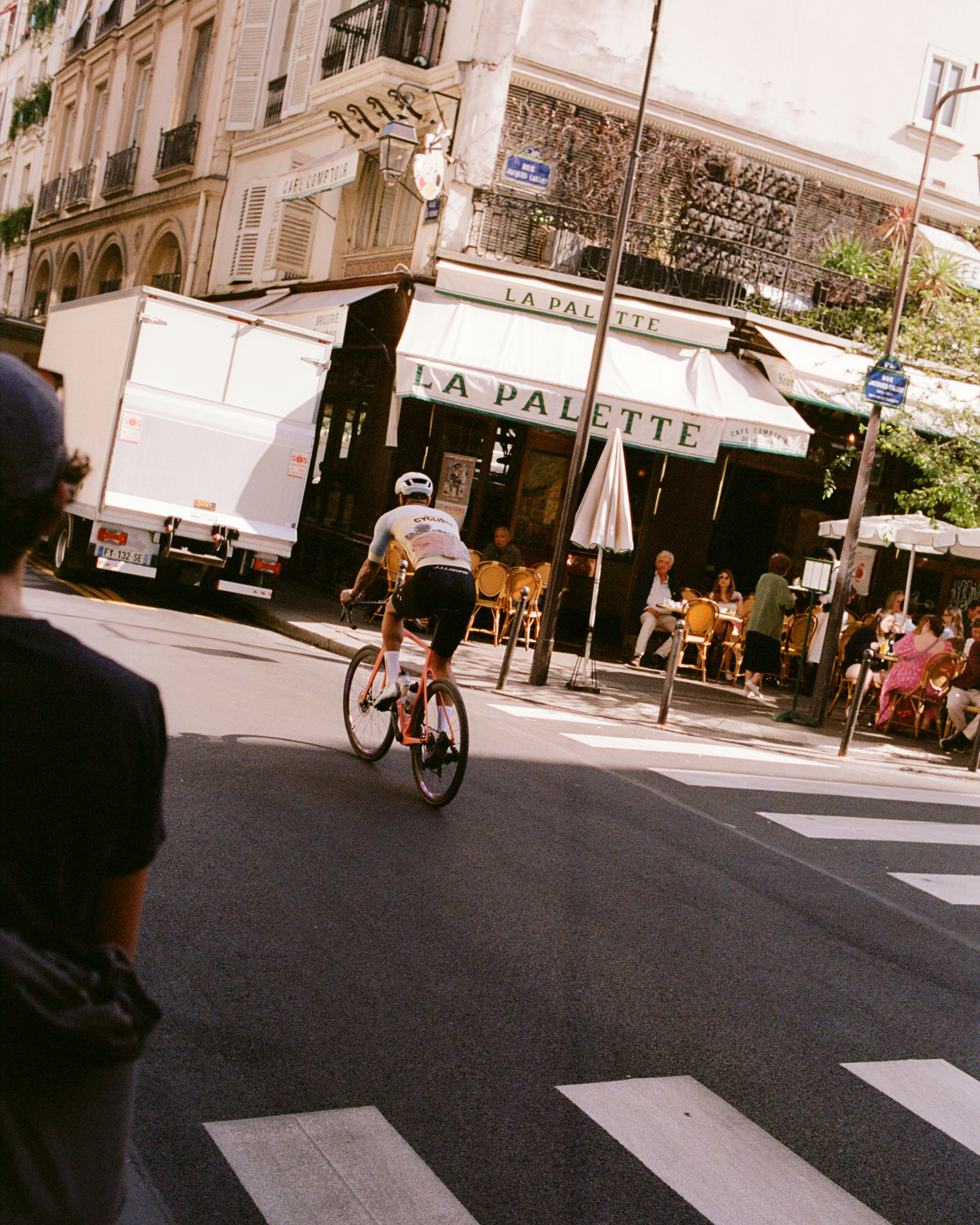 Cyclist in white jersey and black shorts riding through European city street past cafe