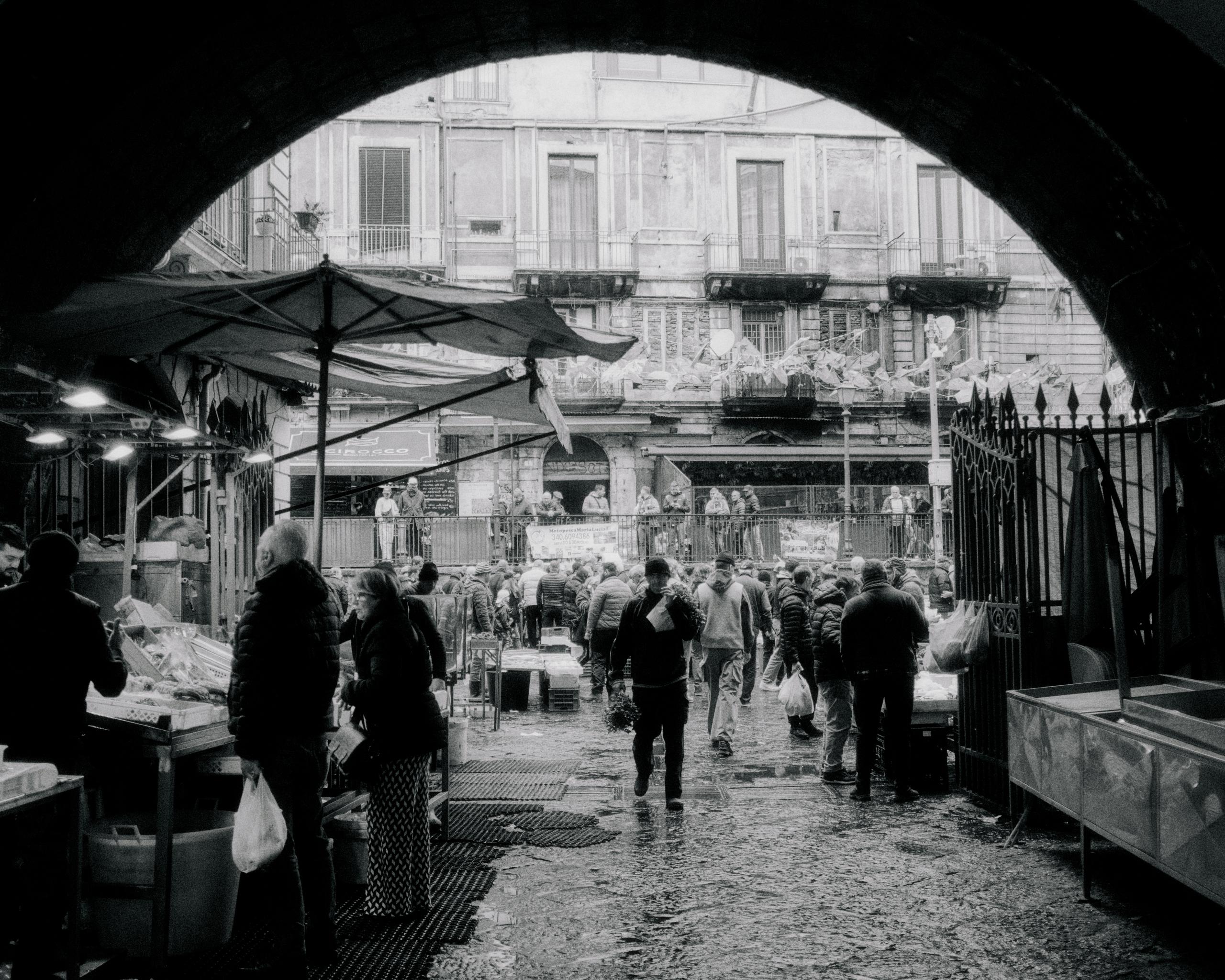 Black and white photo of busy Italian market street with vendors and shoppers under archway