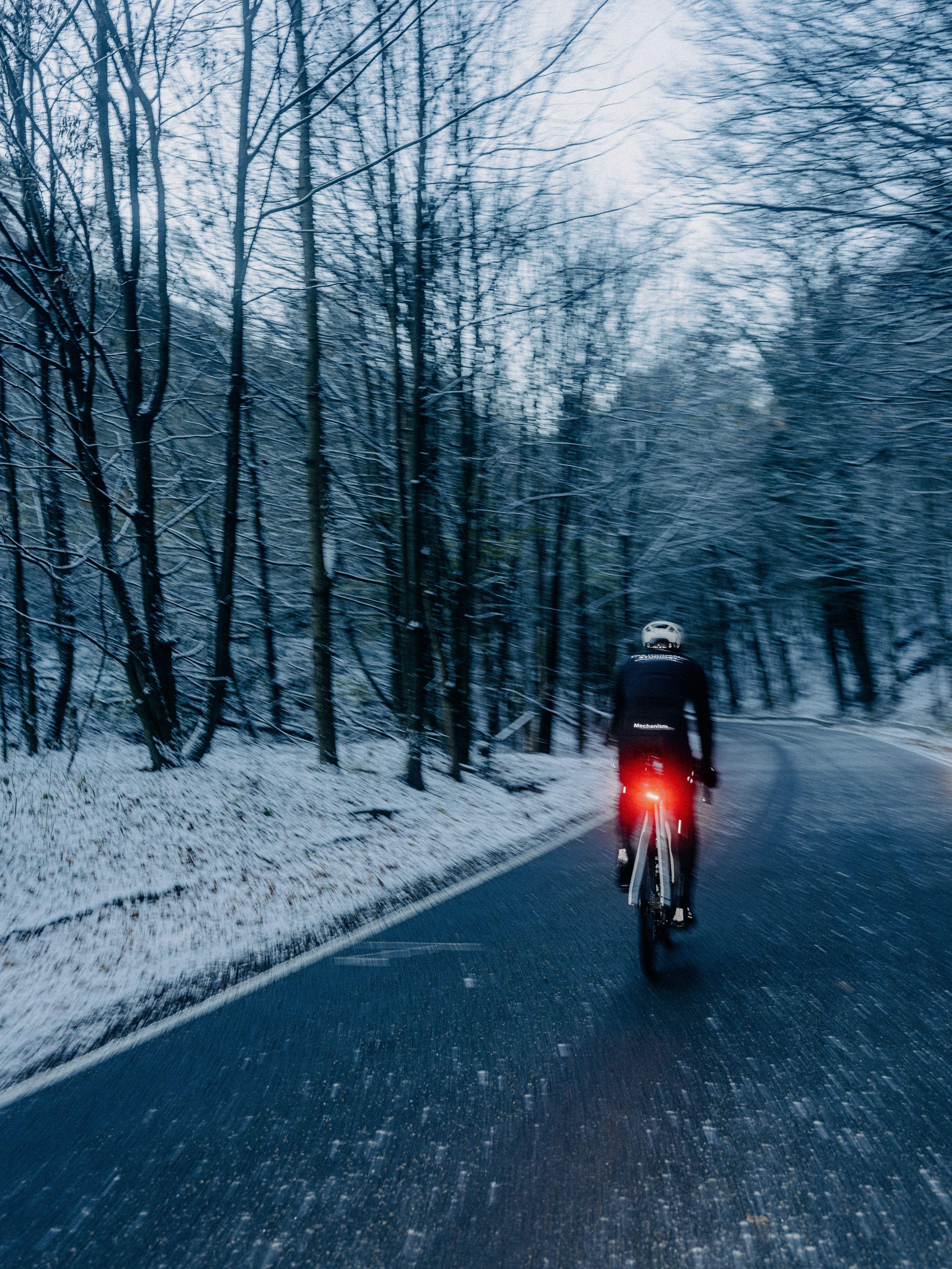 Cyclist riding on snowy forest road at dusk with rear light illuminated