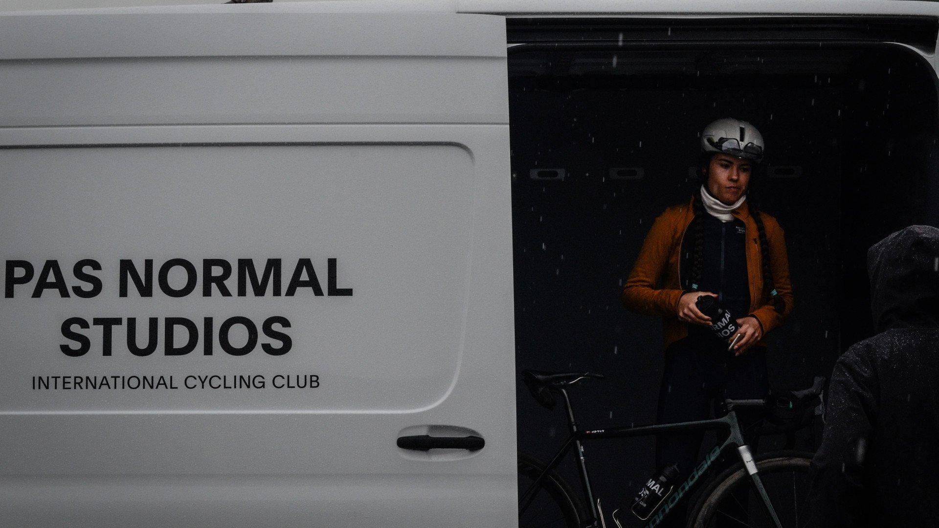 Cyclist with helmet standing beside bike next to branded van in rainy conditions