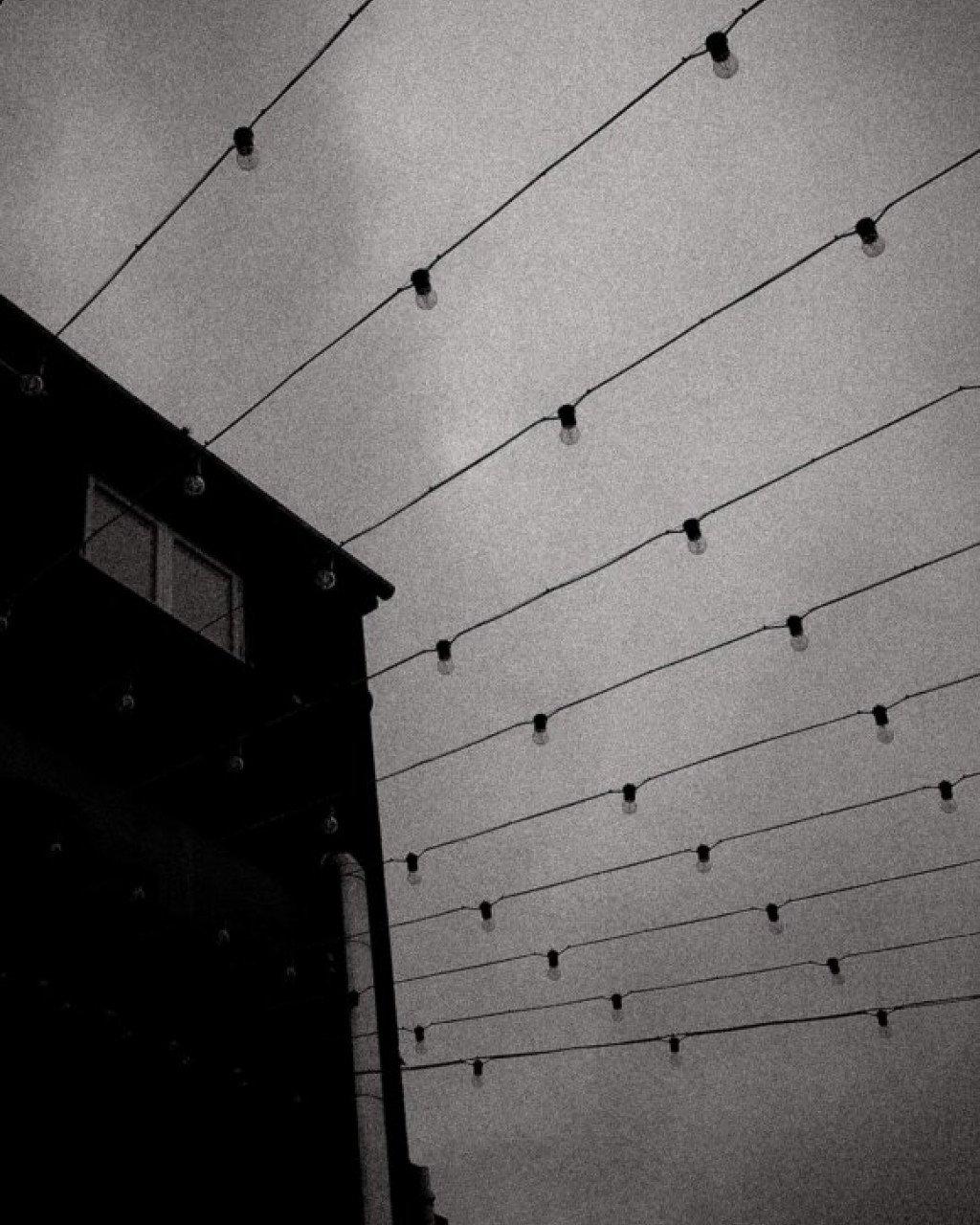 Black and white architectural photo of building corner with overhead string lights against grey sky