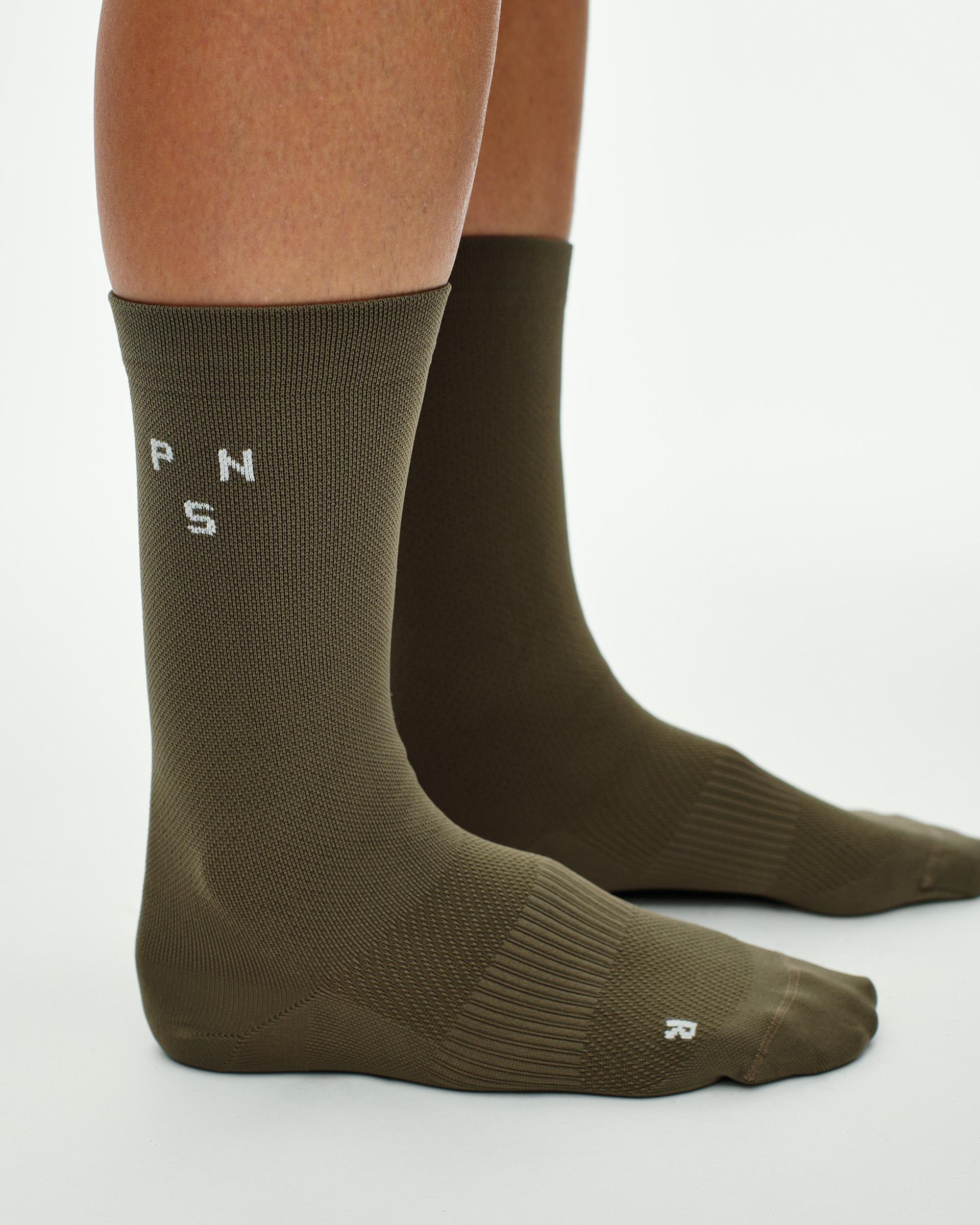 Earth brown Essential cycling socks on model, side view with white PNS logo on cuff
