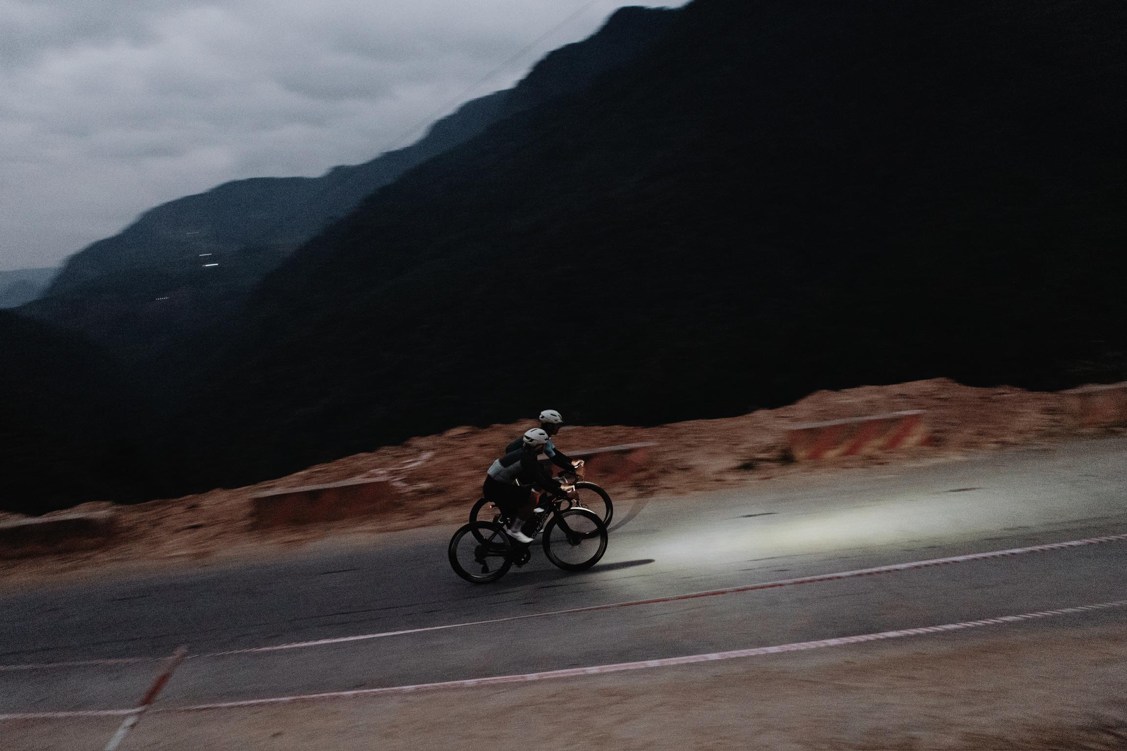 Cyclist in dark apparel riding on mountain road with dramatic valley landscape backdrop