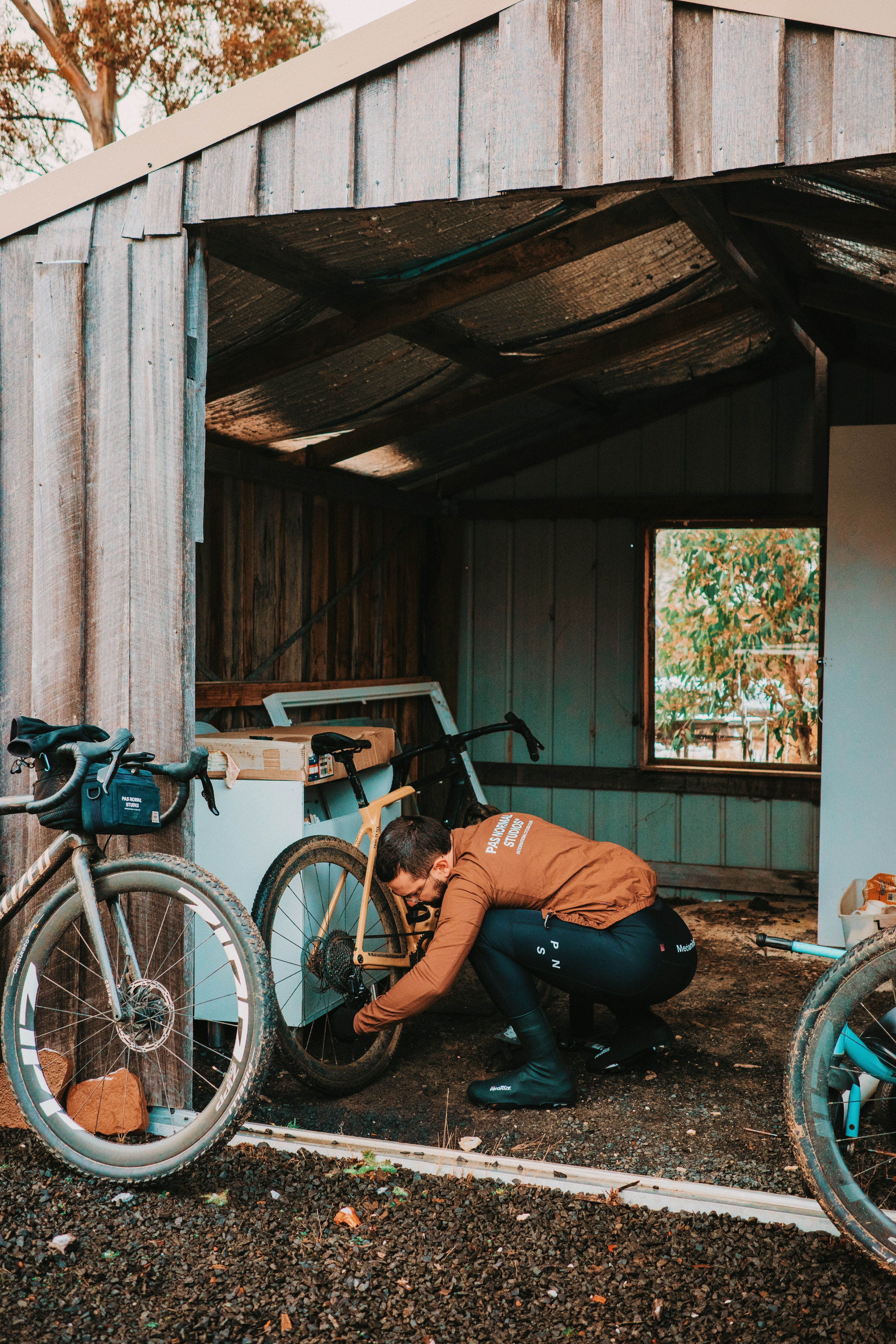 Cyclist in orange jersey maintaining gravel bike outside rustic wooden shed