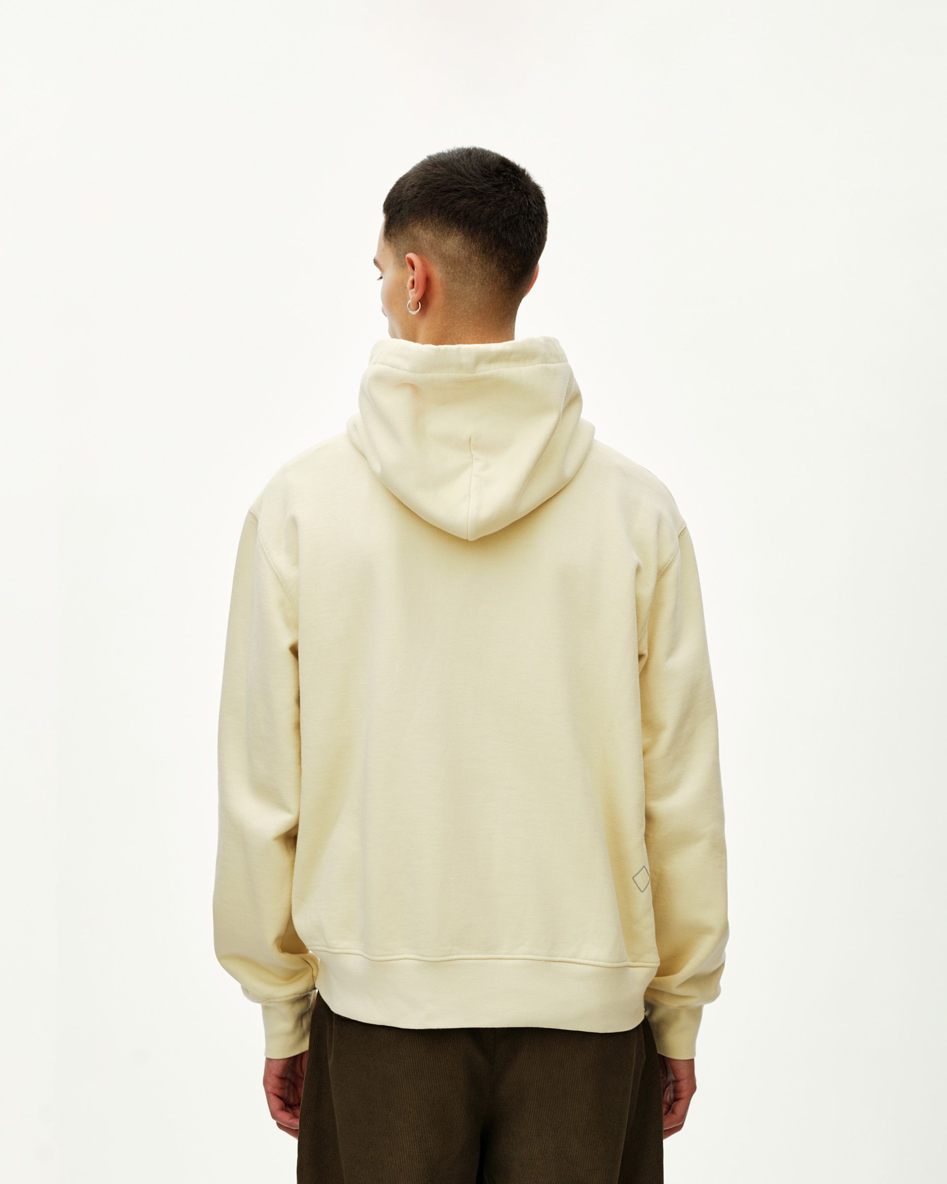 Sand Off-Race hoodie on model, rear view with small diamond logo patch at hem