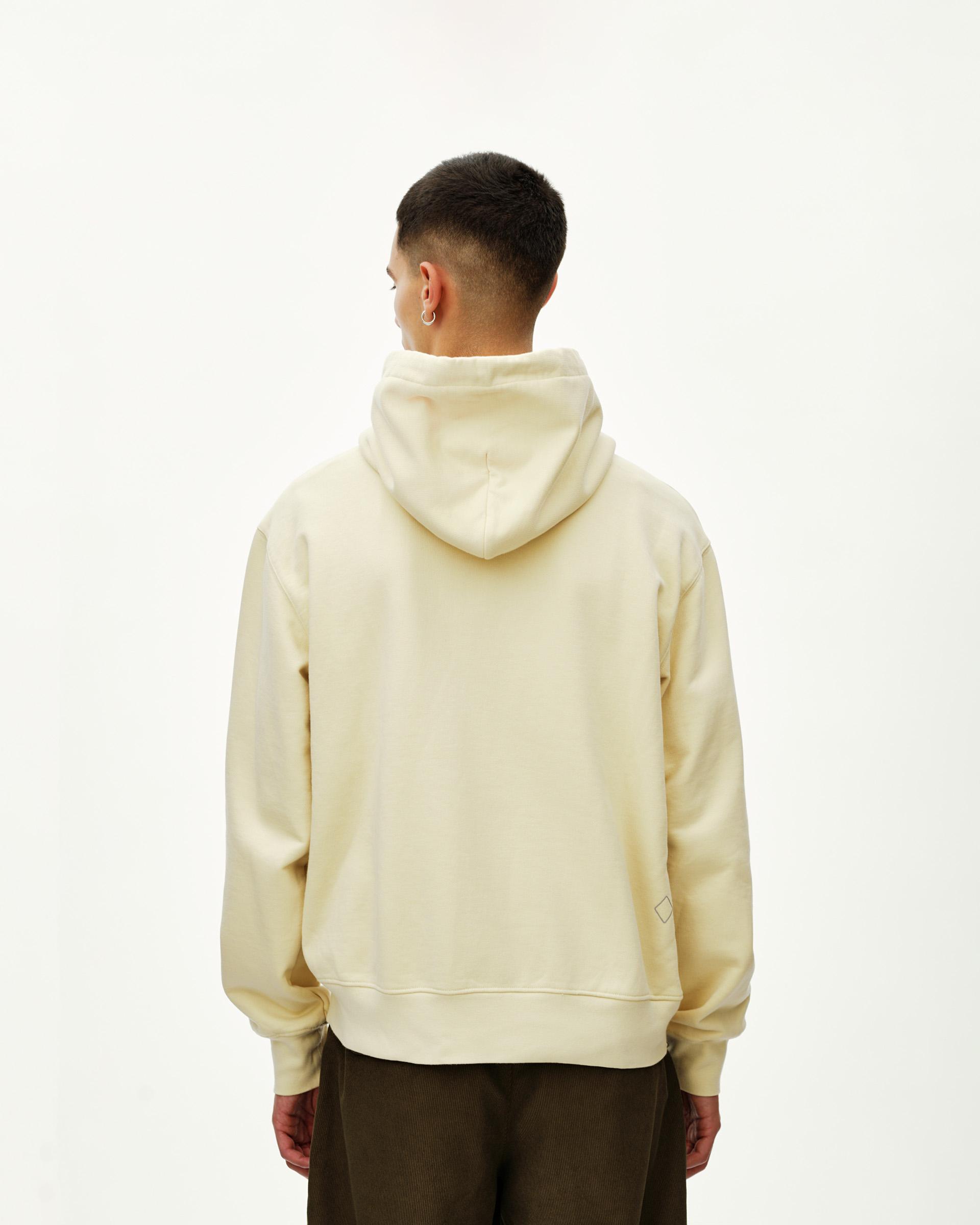 Sand Off-Race hoodie on model, rear view with small diamond logo patch at hem