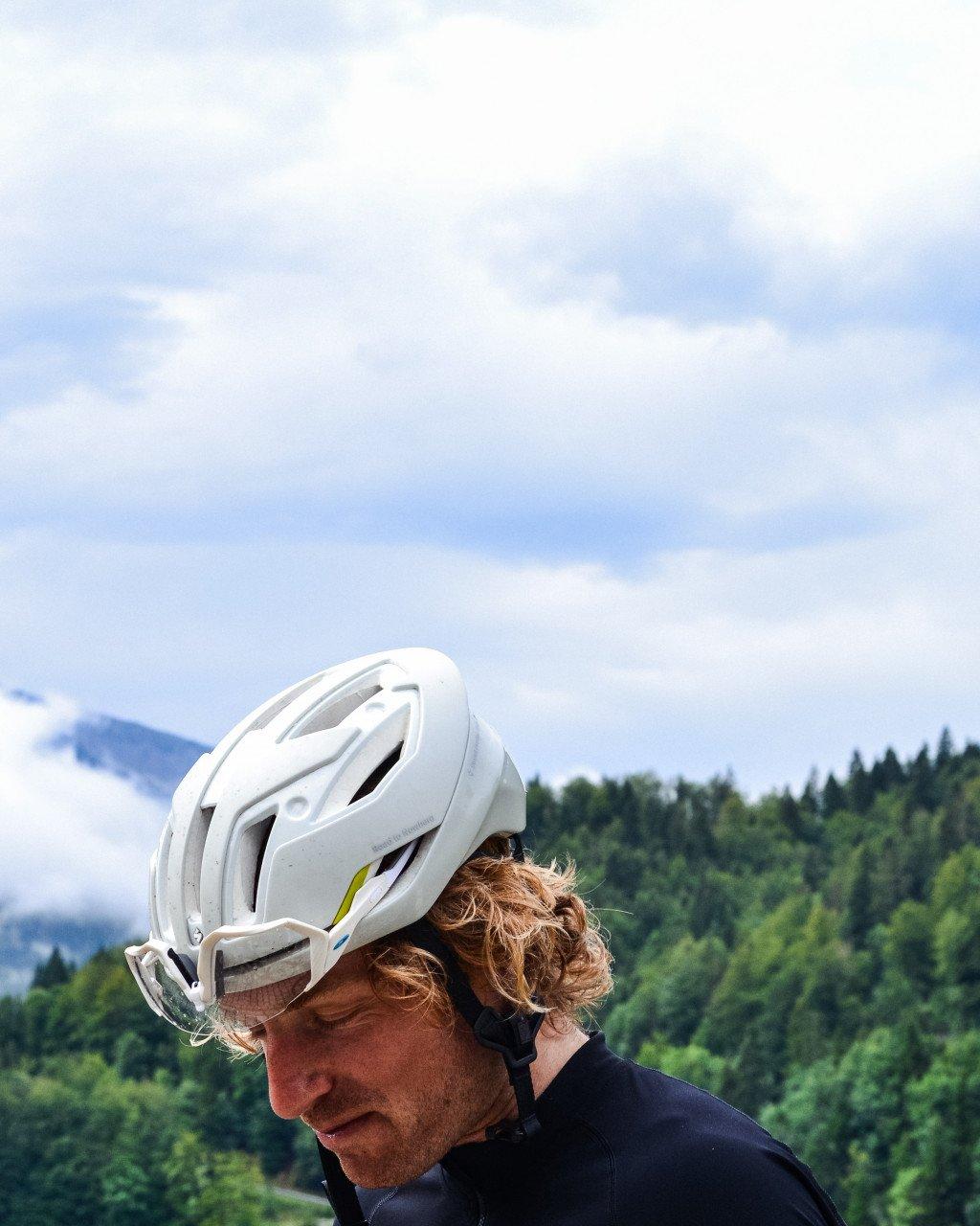 Model wearing white cycling helmet with yellow accents in mountainous forest setting