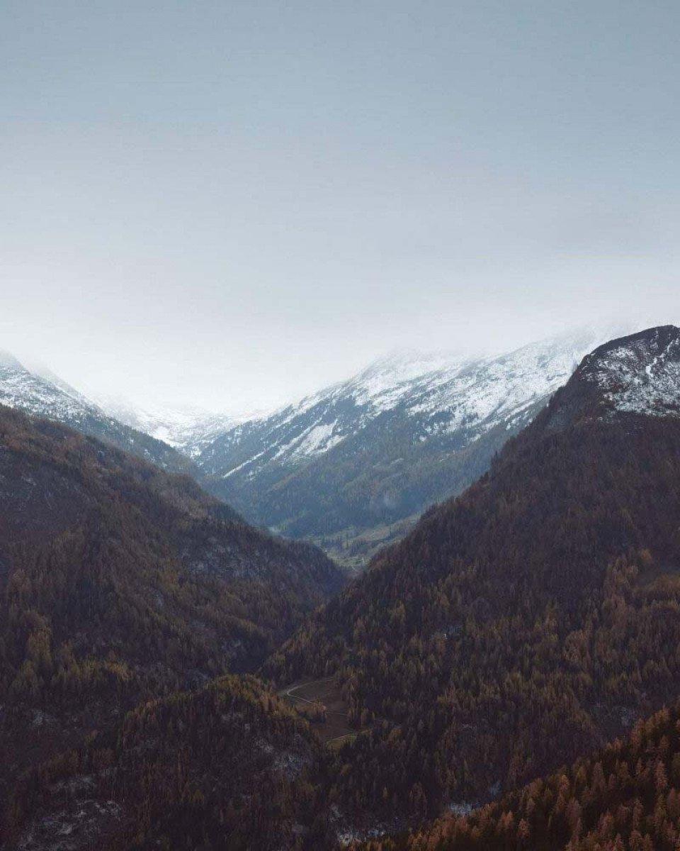 Snow-capped mountain valley with forested hills under overcast sky