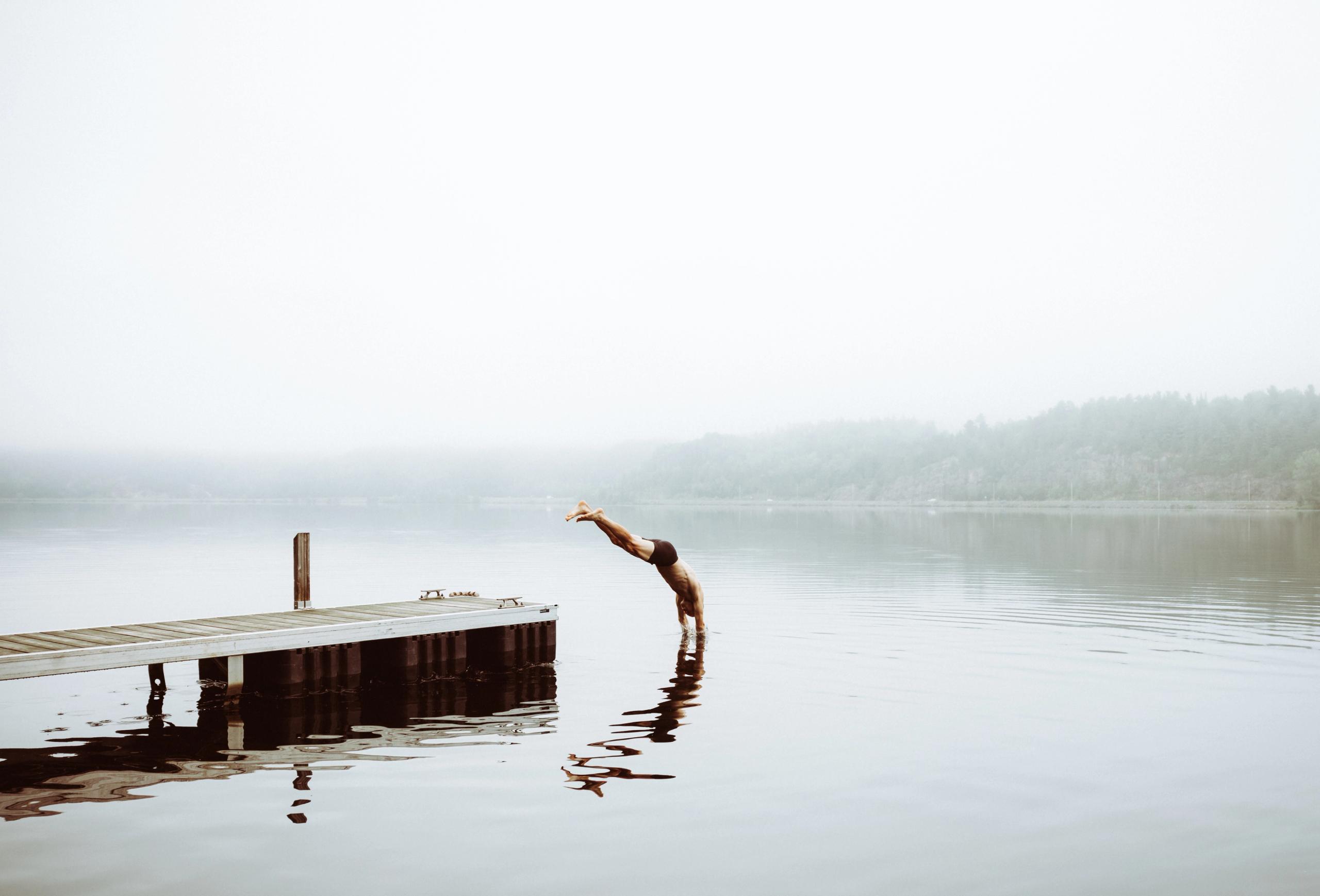 Person diving into misty lake from wooden dock