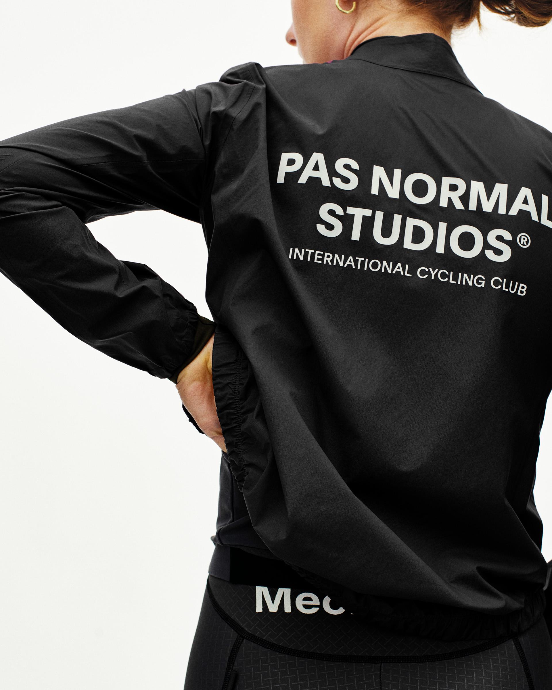Black Mechanism women's cycling rain jacket on model, rear view with large white logo print