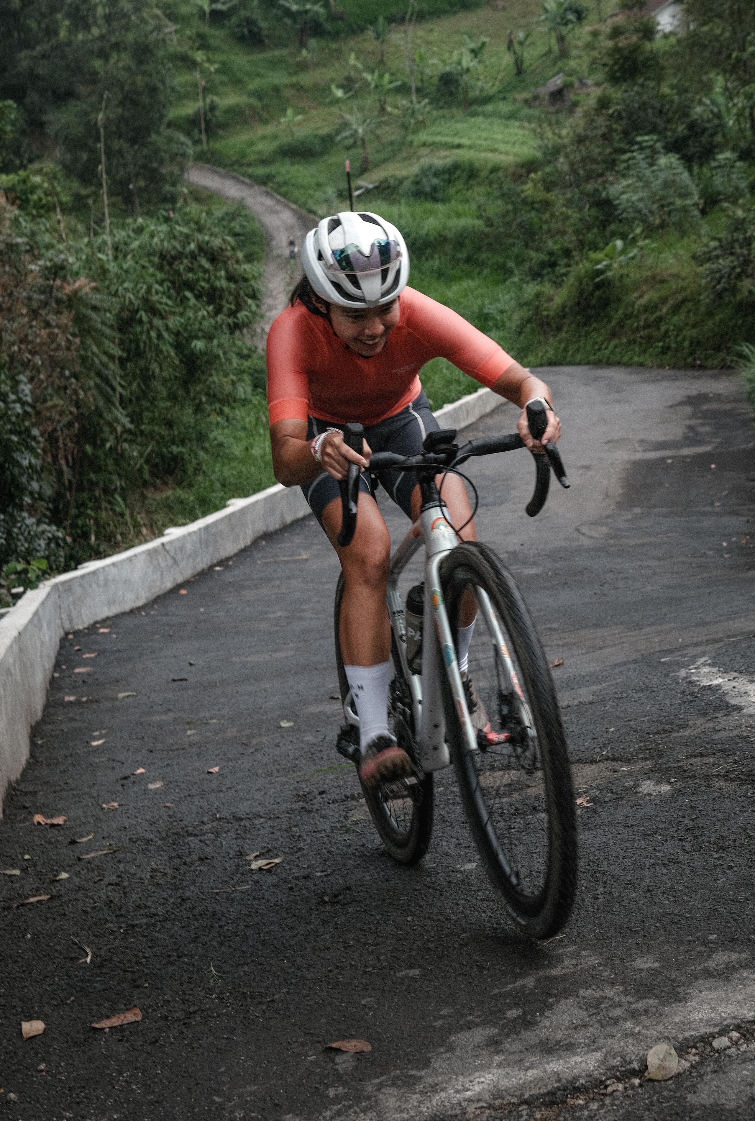Model wearing red long-sleeve cycling jersey on time trial bike descending mountain road