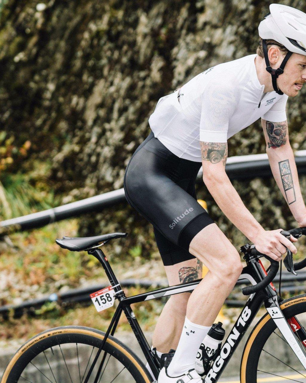 Model wearing white Solitude Aero Jersey and black bib shorts in aerodynamic cycling position on time trial bike