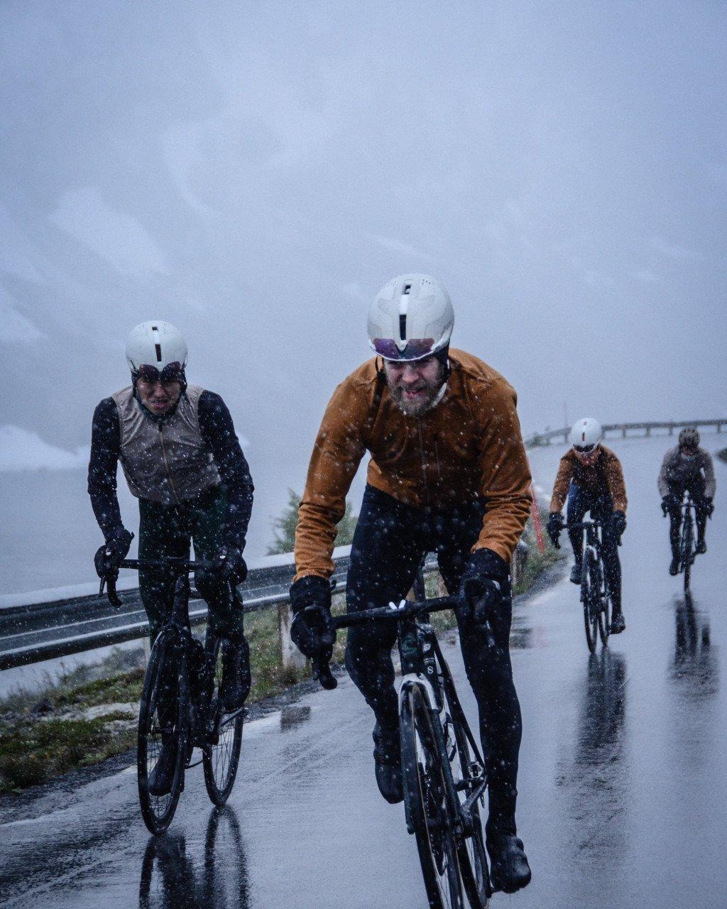 Cyclists riding time trial bikes on wet road in falling snow wearing aerodynamic helmets and winter cycling gear
