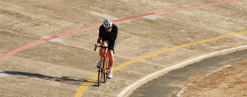 Cyclist in black jersey on orange time trial bike riding on velodrome track