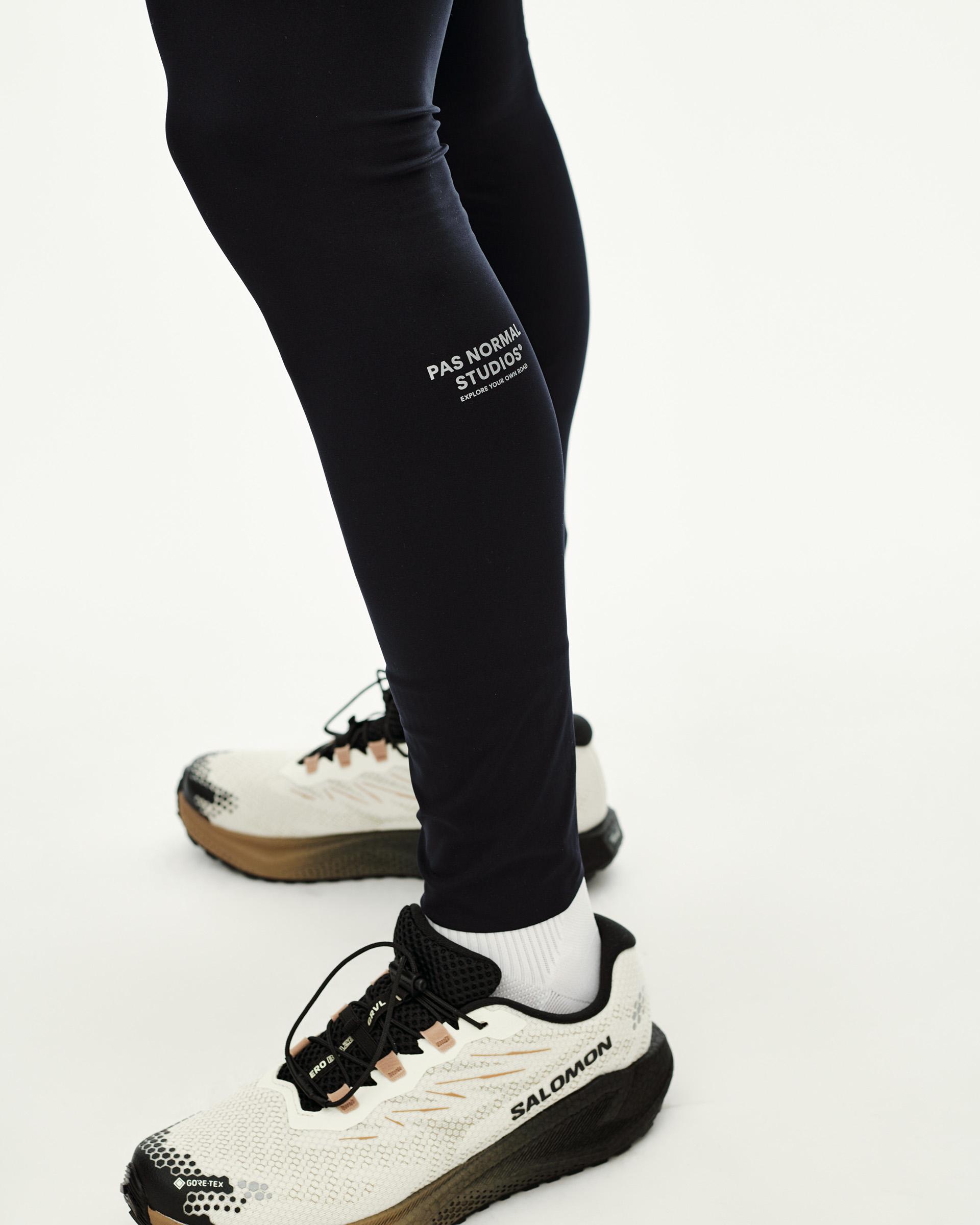 Black Balance long tights on model, side detail view with white logo print on lower leg