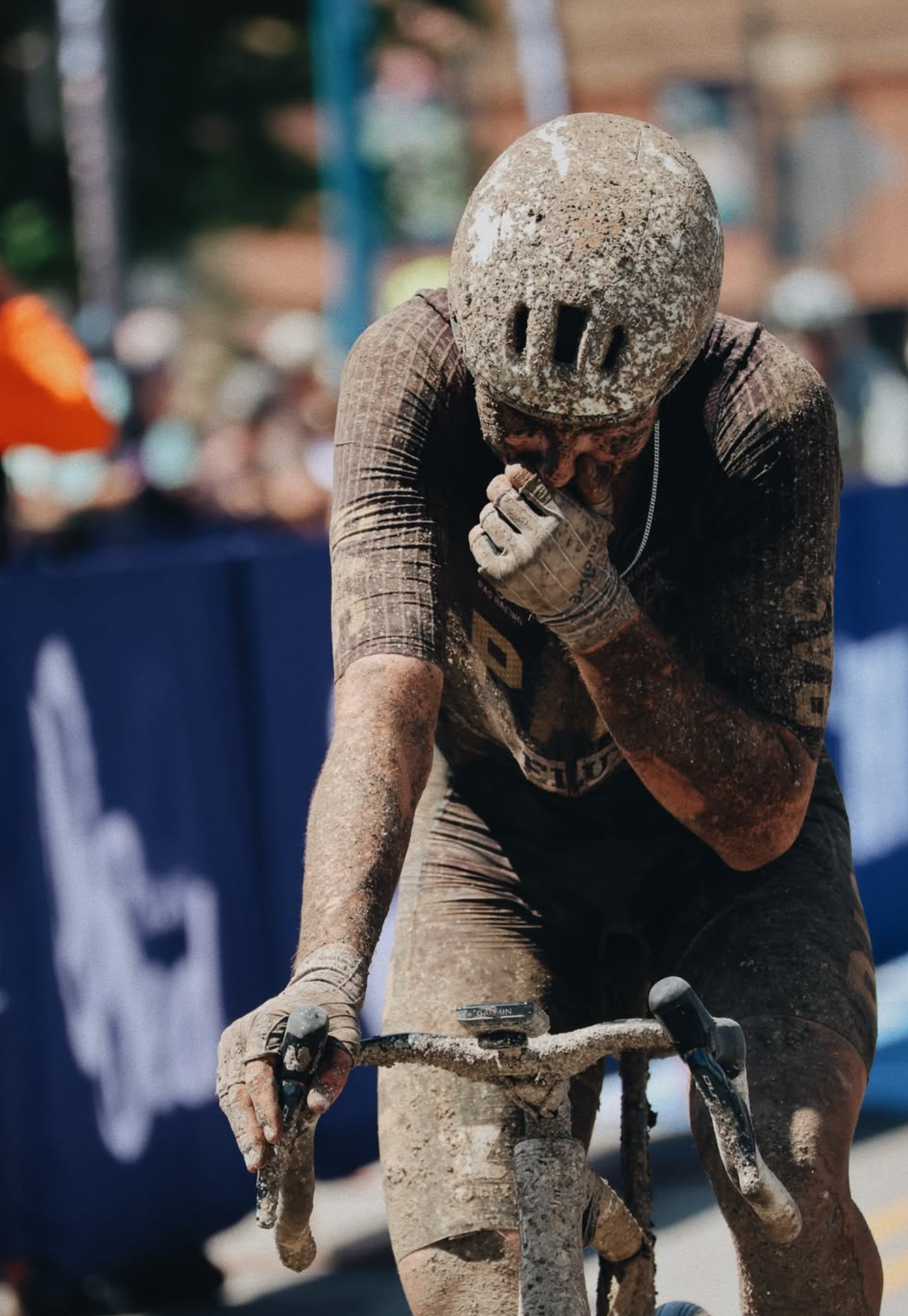 Model wearing mud-covered cycling outfit in aerodynamic position during gravel race