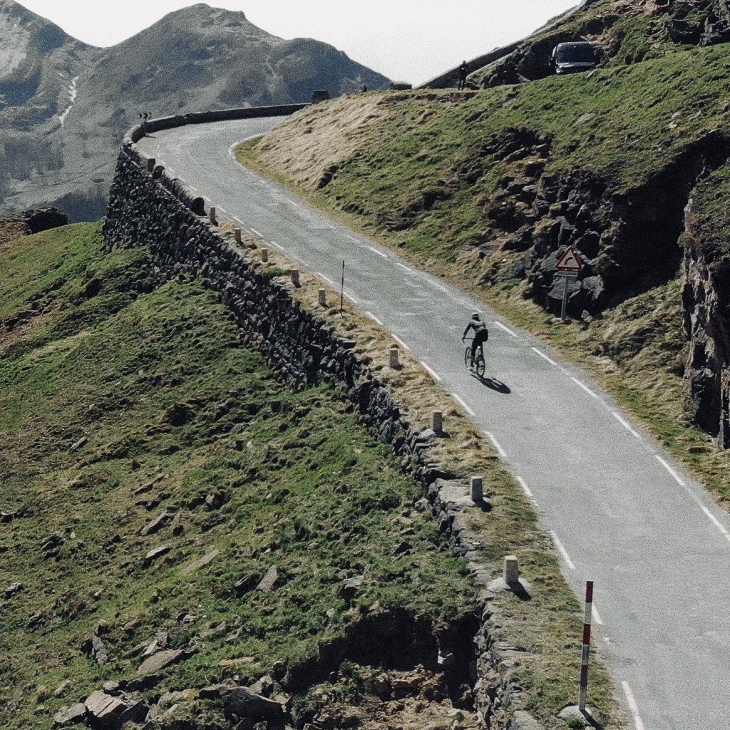 Cyclist on winding mountain road with stone walls and green hillsides