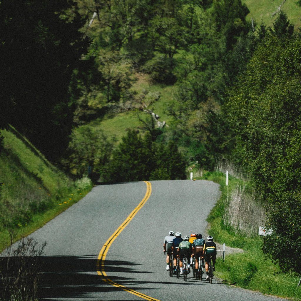Group of cyclists riding on winding road through green hills in Sonoma