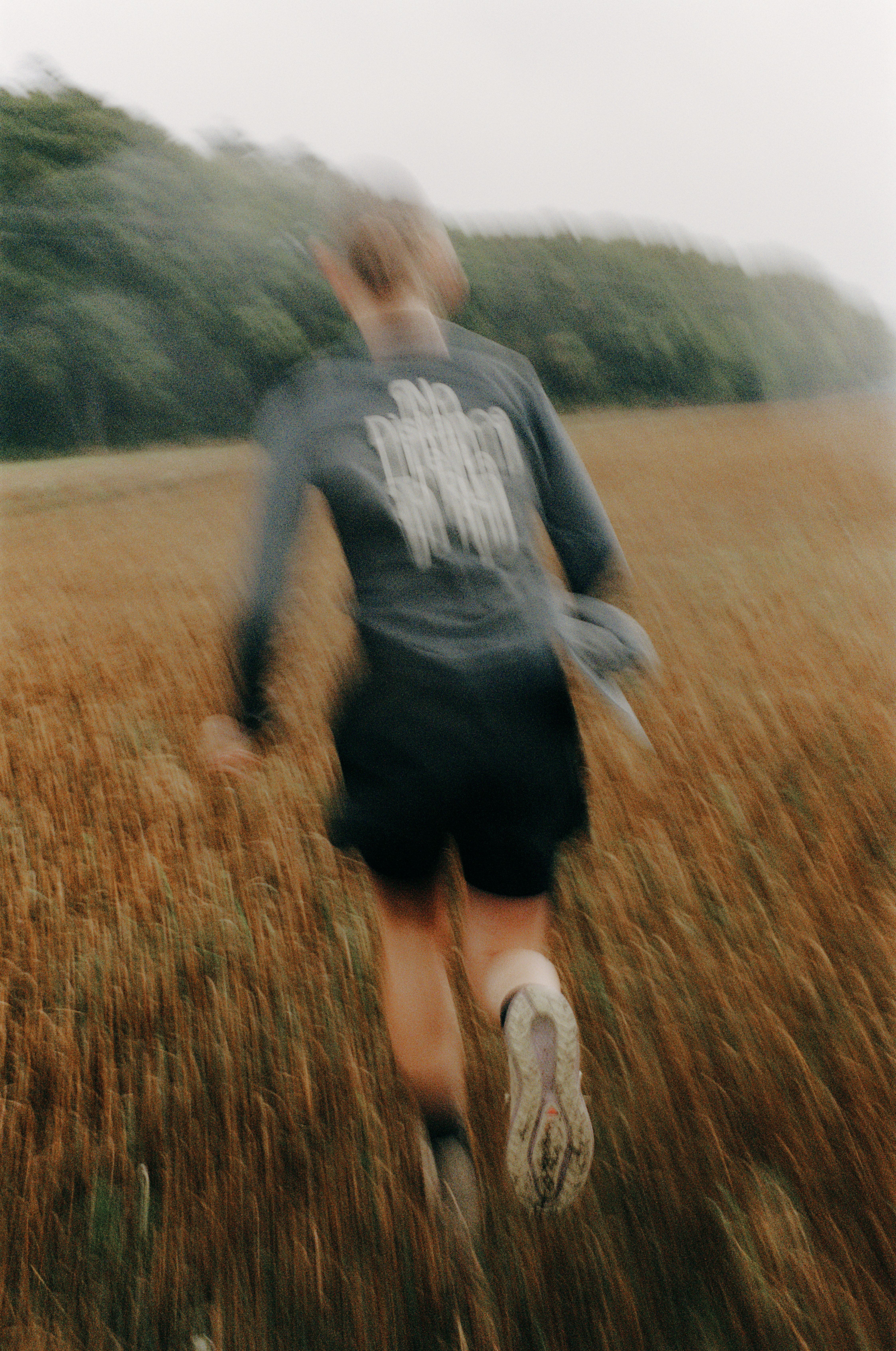 Model wearing dark running shorts and grey t-shirt with white chest lettering, running through golden field