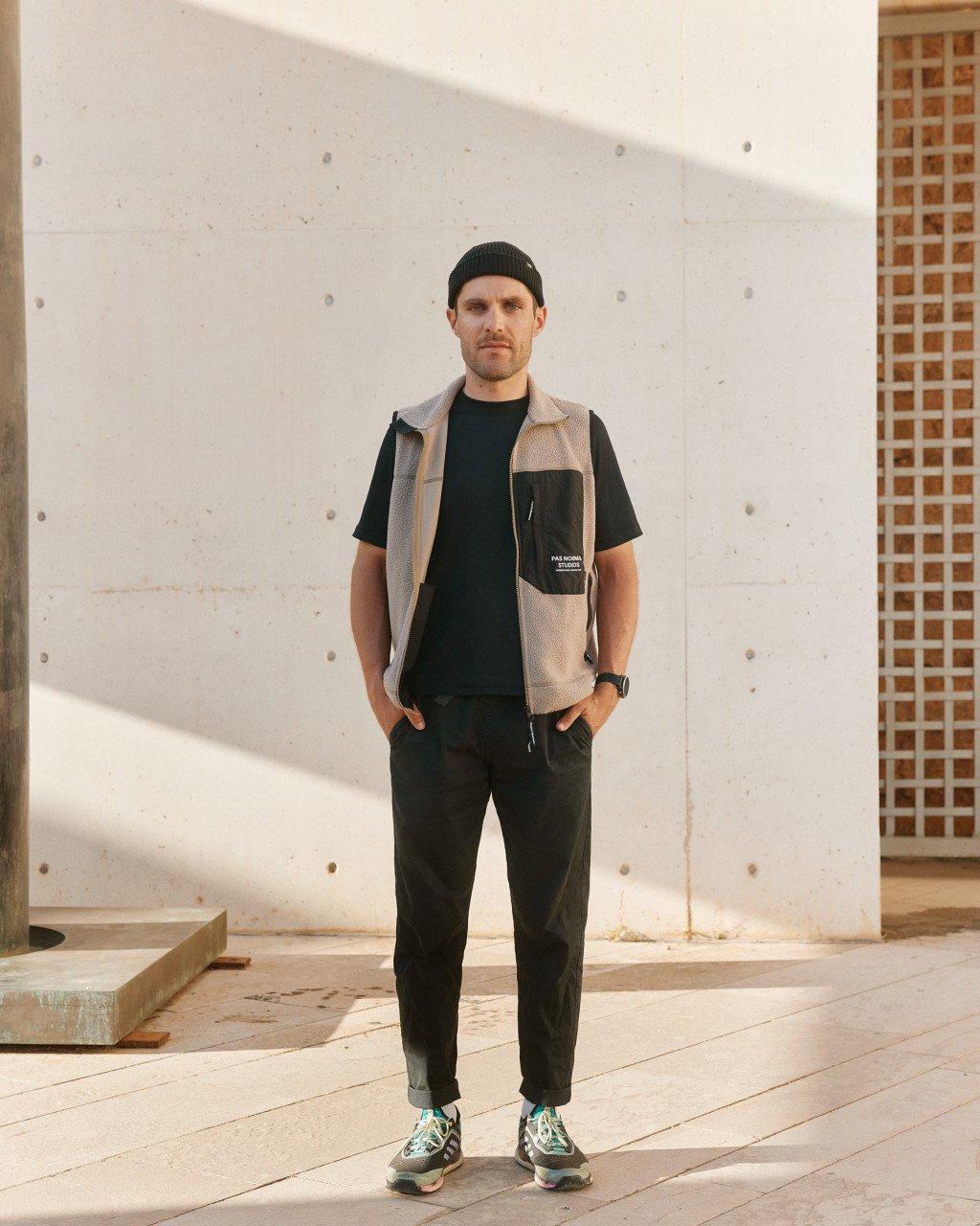 Model wearing beige fleece vest over black t-shirt with chest pocket and black jogger pants