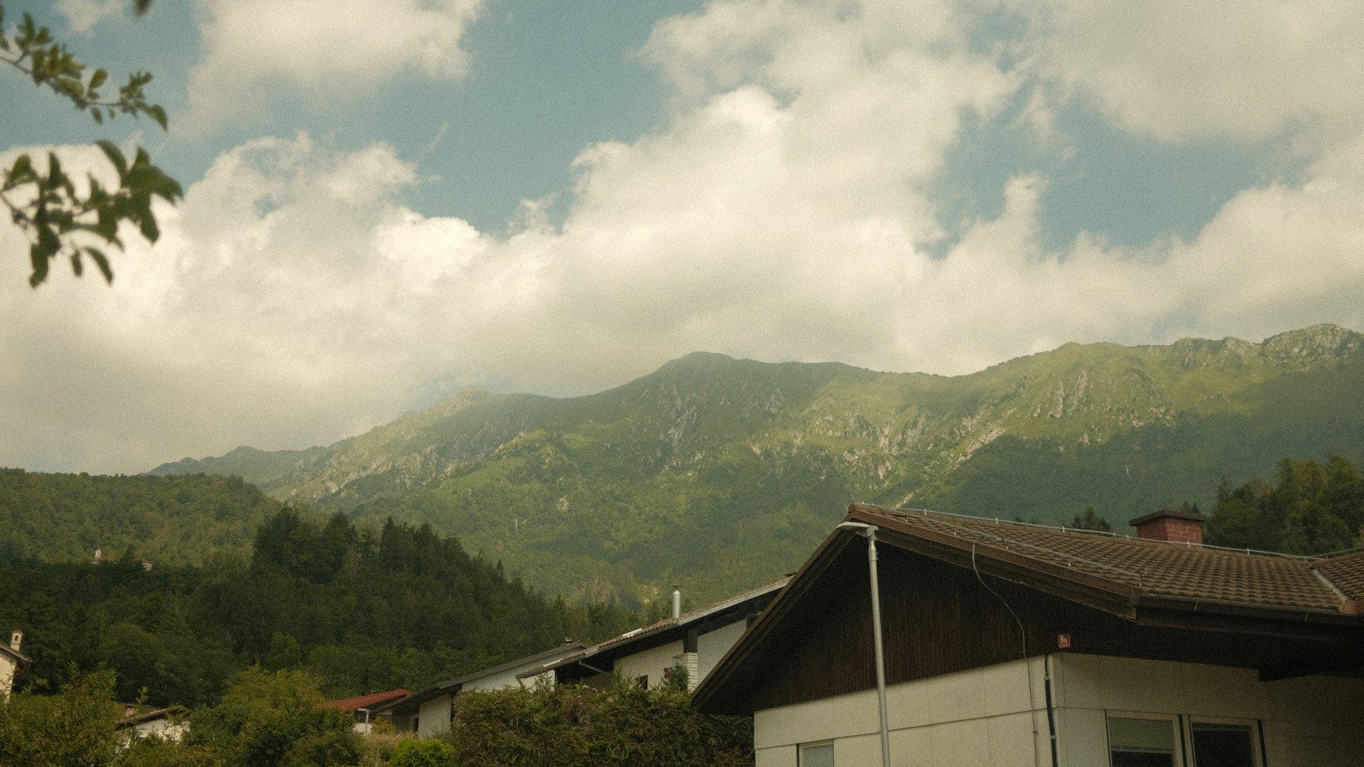 Mountain landscape view with traditional Alpine houses and forested hills under cloudy sky in Slovenia